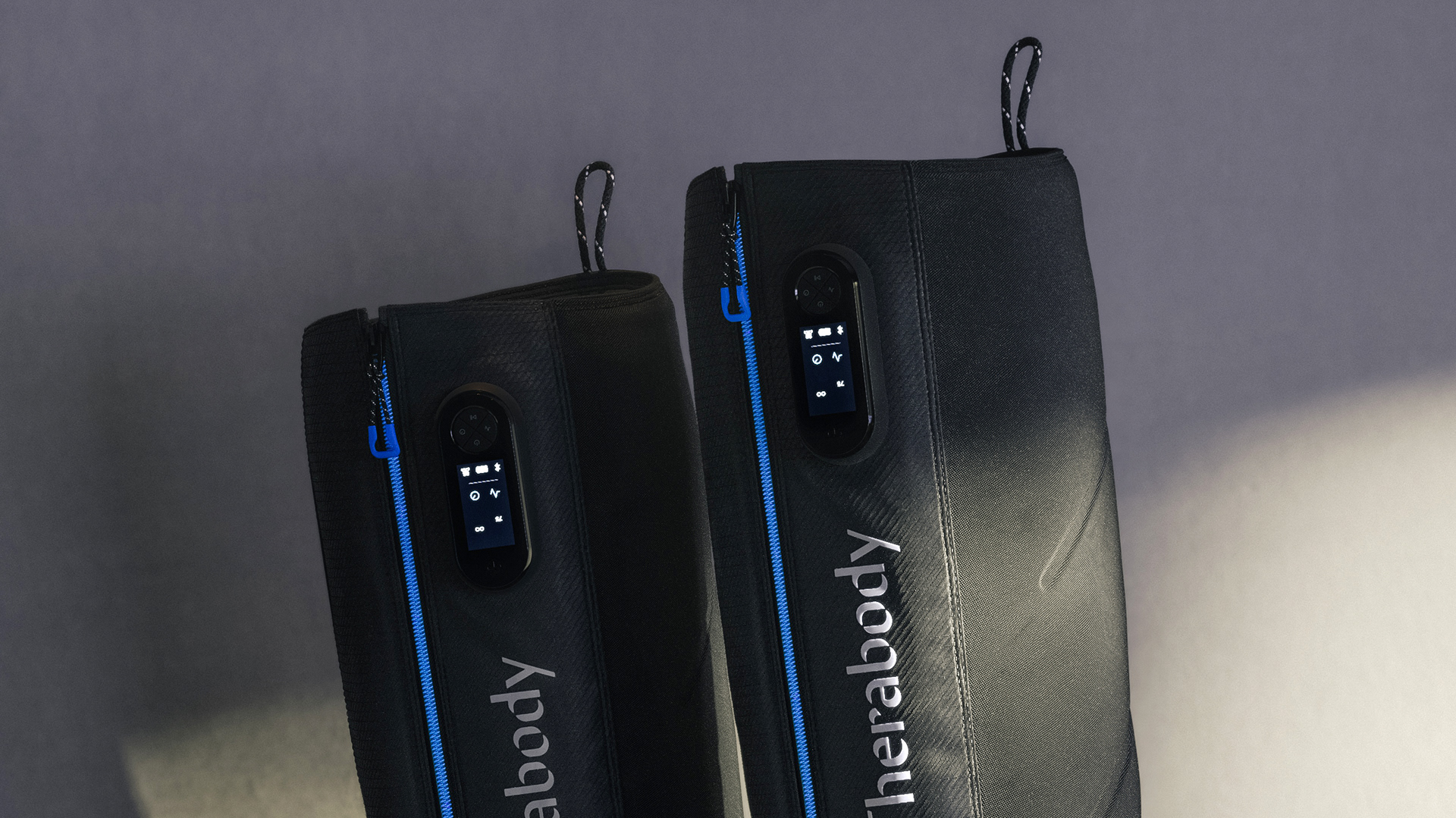 Two black Therabody Jetboots side by side, with one showing the control panel and the other displaying the brand name.