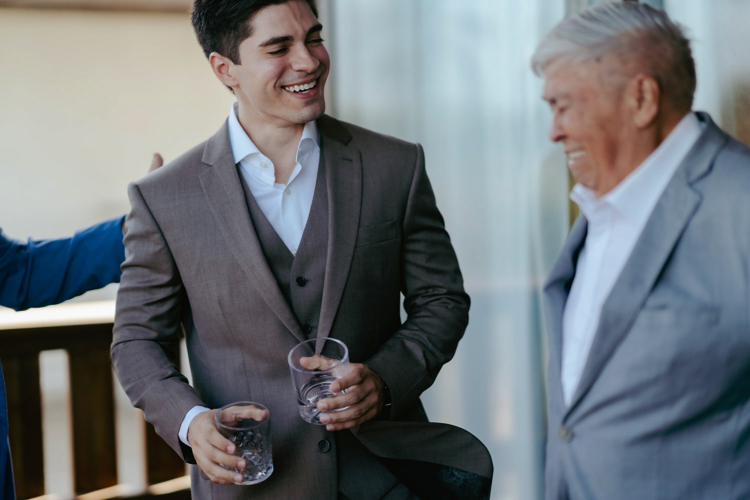Momento espontâneo do noivo rindo e brindando com pai/convidado antes da cerimônia de casamento. Registro de Rebeca Santos na praia de Barra Grande, litoral do Piauí.