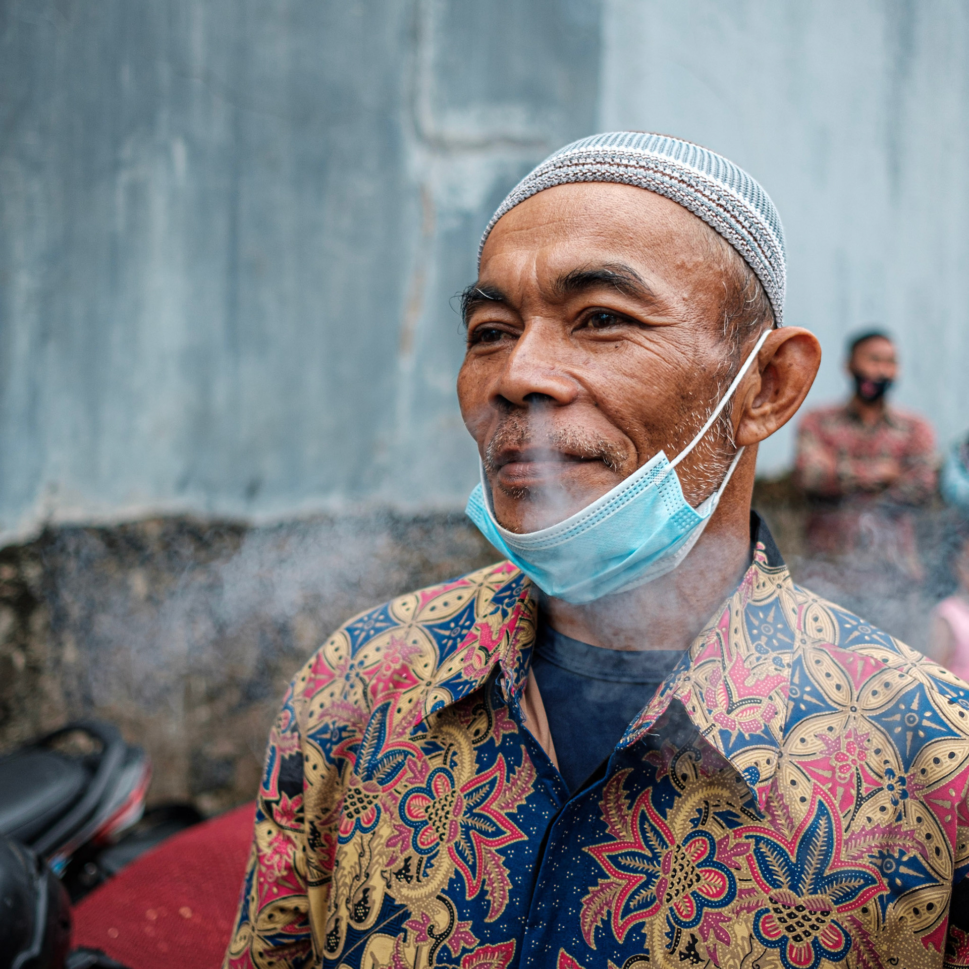 man in orange blue and yellow floral button up shirt wearing white taqiyah cap