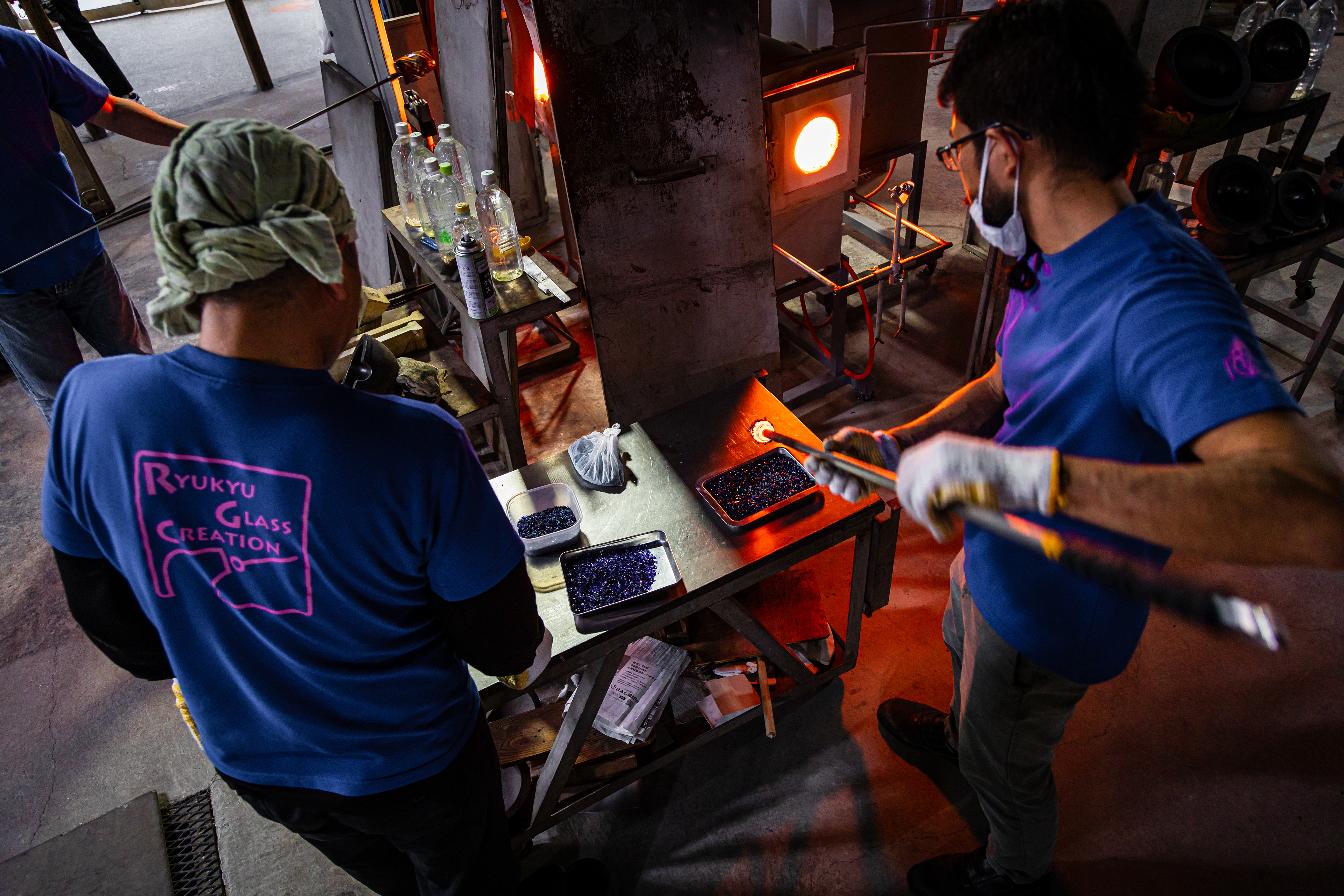 Glass artists at the Ryukyu Glass Village factory dip molten glass in small colored fragments, creating Ryukyu Glassware's distinctive vibrant colors.