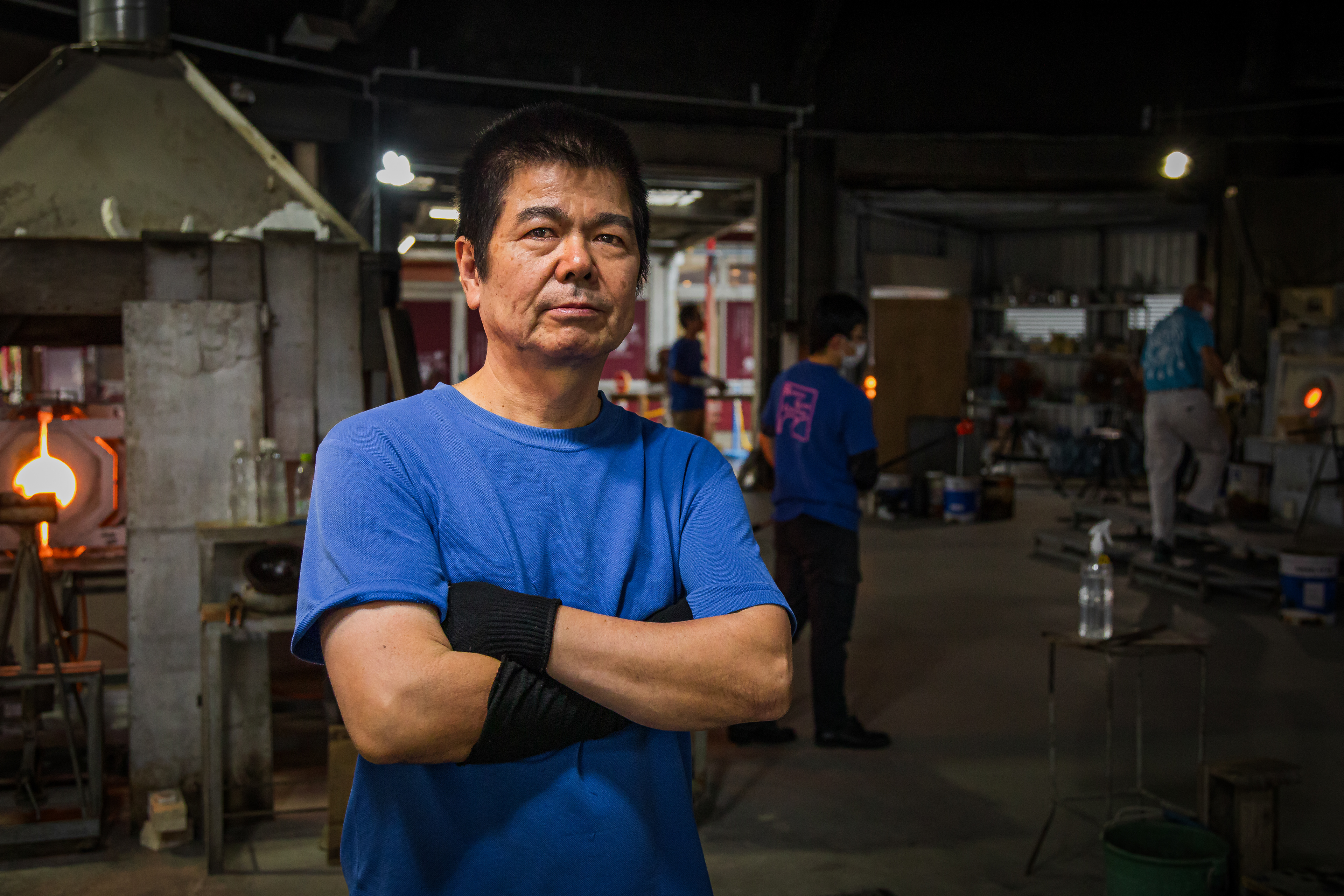 Mr. Sueyoshi, one of the many glass-blowing artisans, poses for a portrait inside of the Ryukyu Glass Village factory. 