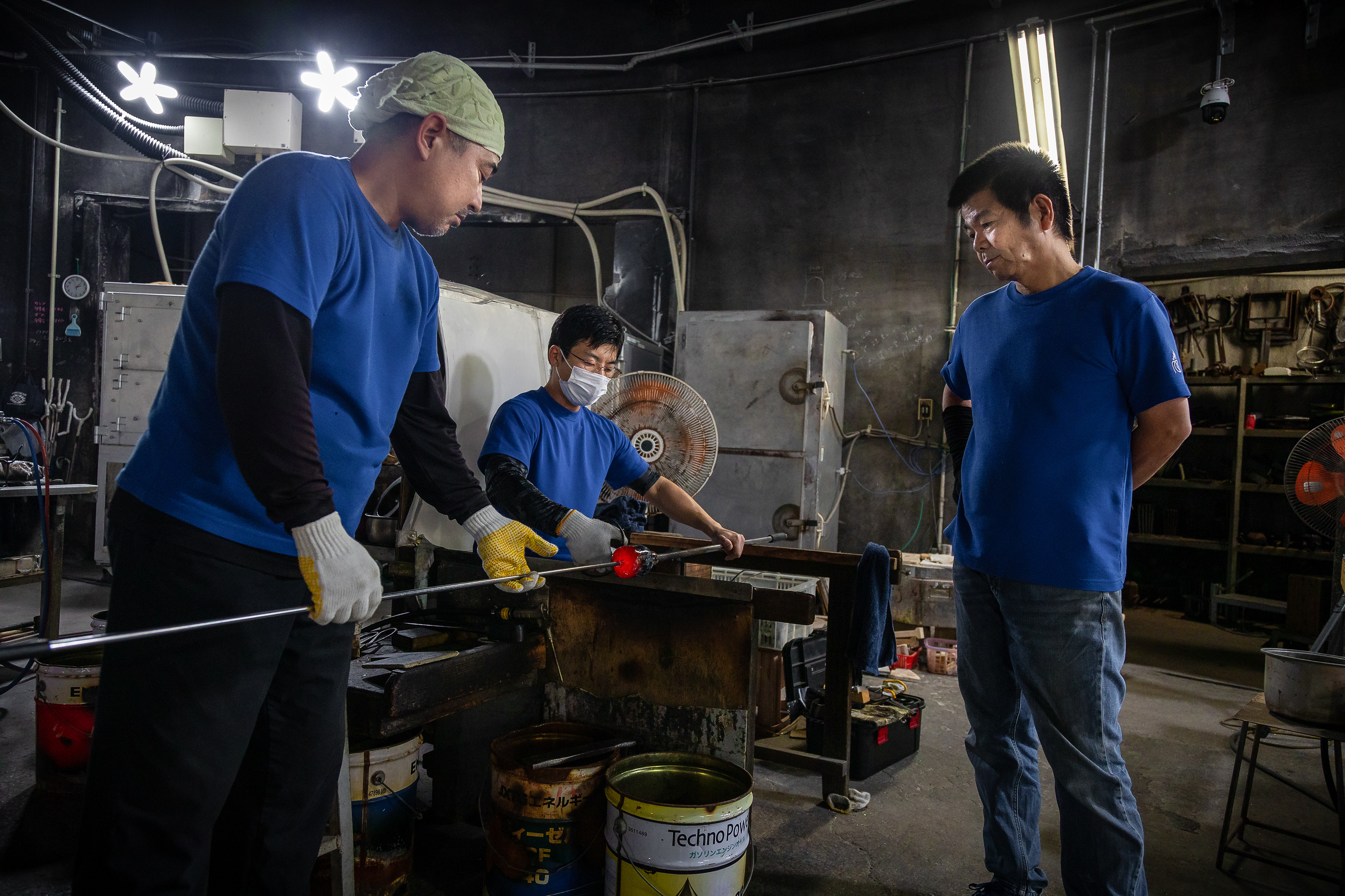 Glassblowing artisans at Ryukyu Glass Village craft vibrant glass products in a workshop, utilizing a kiln reaching 2372 F (1300 C). Amid their creative process, the workshop's internal temperature can soar up to 105 F (40 C). This artistic endeavor involves shaping molten glass by blowing air through a blowpipe, resulting in items such as cups, plates, bowls and more, enhanced with color and meticulous shaping.