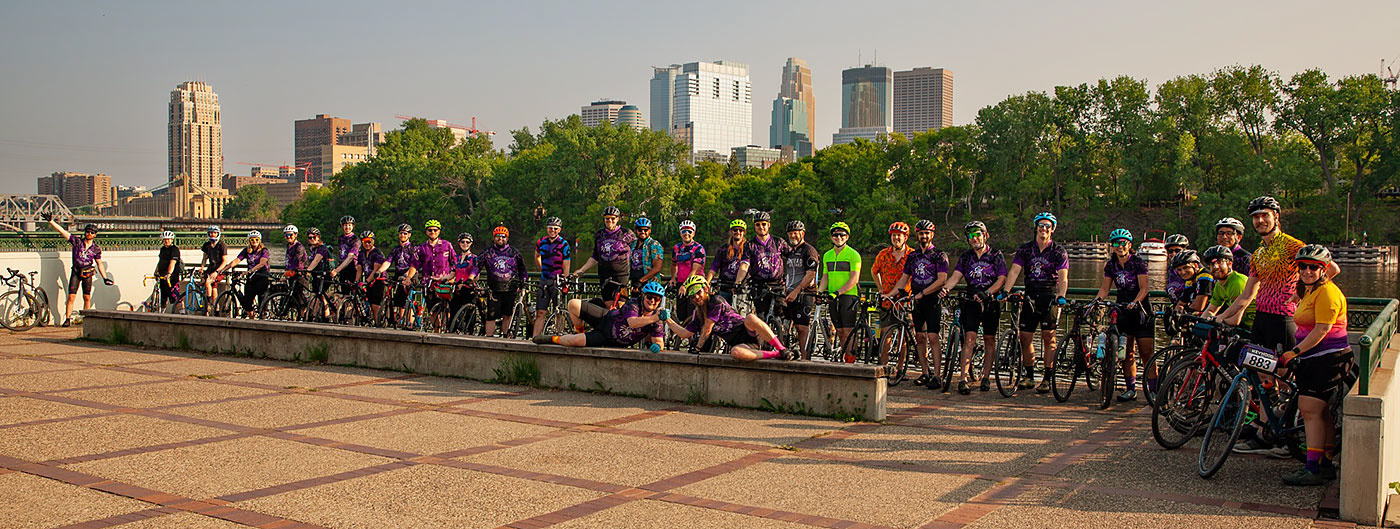 33 cyclists stand next to their bikes with the Minneapolis skyline in the background