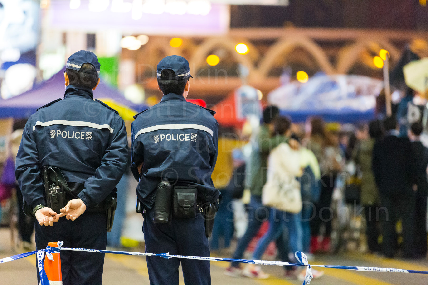 HONG KONG, CHINA - 14 December 2014: Police watch people at a crowd control cordon line during the Umbrella Protest, so named for the the use of umbrellas to resist Police use of pepper spray to disperse the crowd during a 79-day occupation of the city demanding more transparent elections.