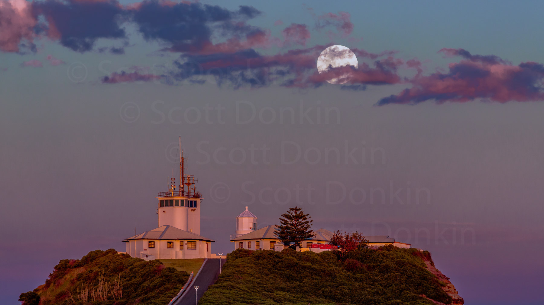 NEWCASTLE, NSW, AUSTRALIA - 3 December 2017:  As the sun fades on the opposite horizon, a bright perigee Moon rises over Nobby's Lighthouse and Promontory. Waxing, 99.8% disc illumination. Single exposure.