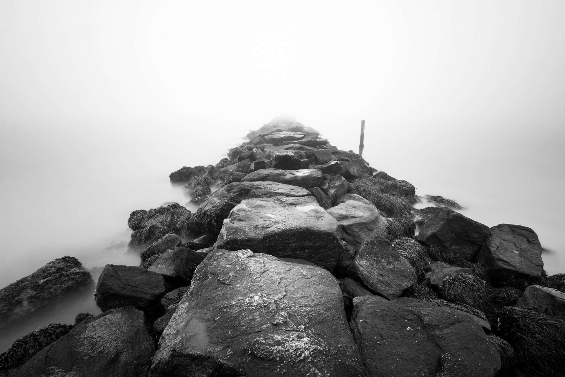 Black and white long exposure of a breakwall receding into the ocean.