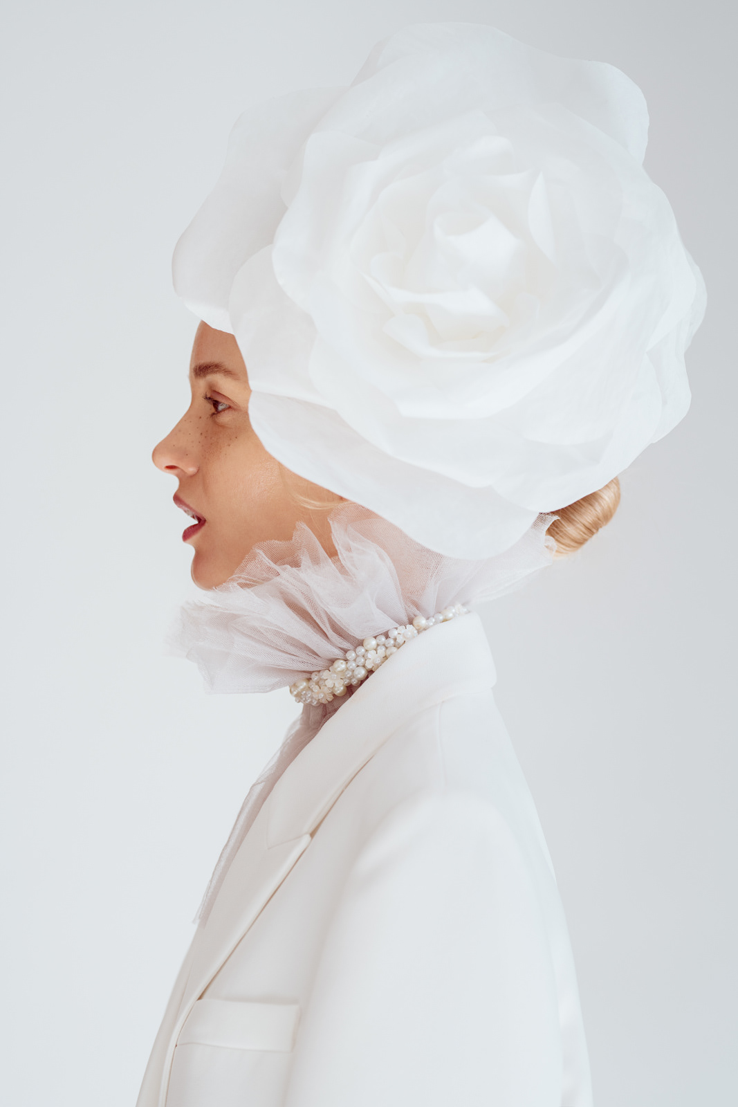 Studio beauty portrait of model in white suit with oversized flower headpiece – Joanna Kustra creative editorial photography