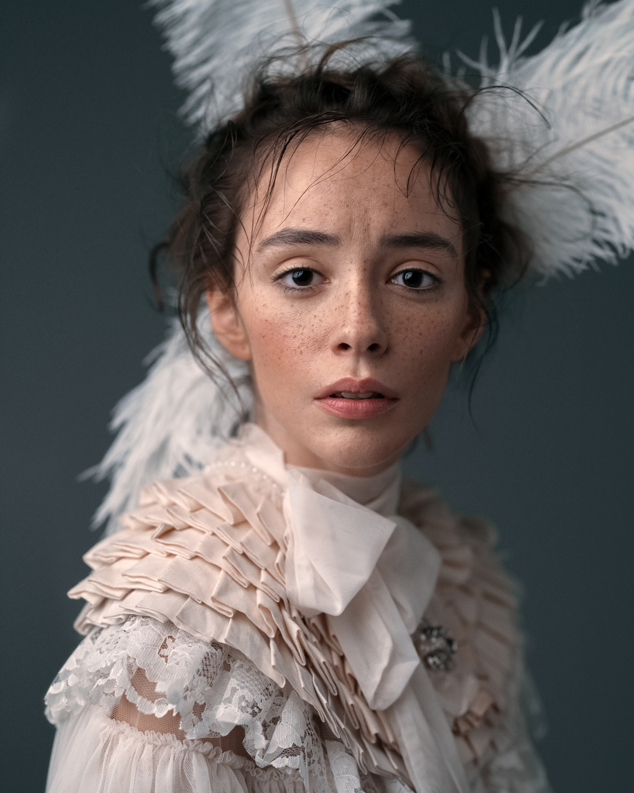 Editorial portrait of freckled model in white ruffled blouse with feathered headpiece – Joanna Kustra fine art photography