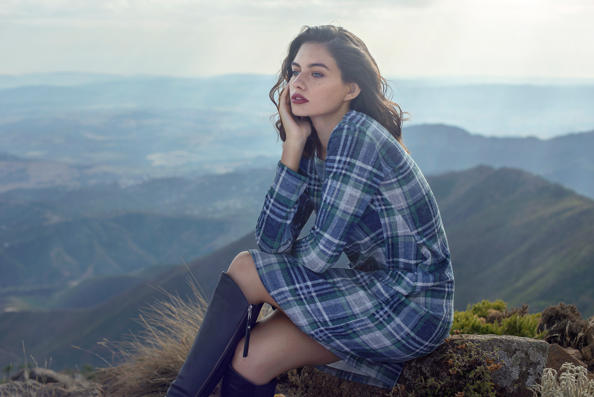 Editorial outdoor portrait of model in plaid dress with knee-high boots against mountain backdrop – Joanna Kustra destination fashion photography