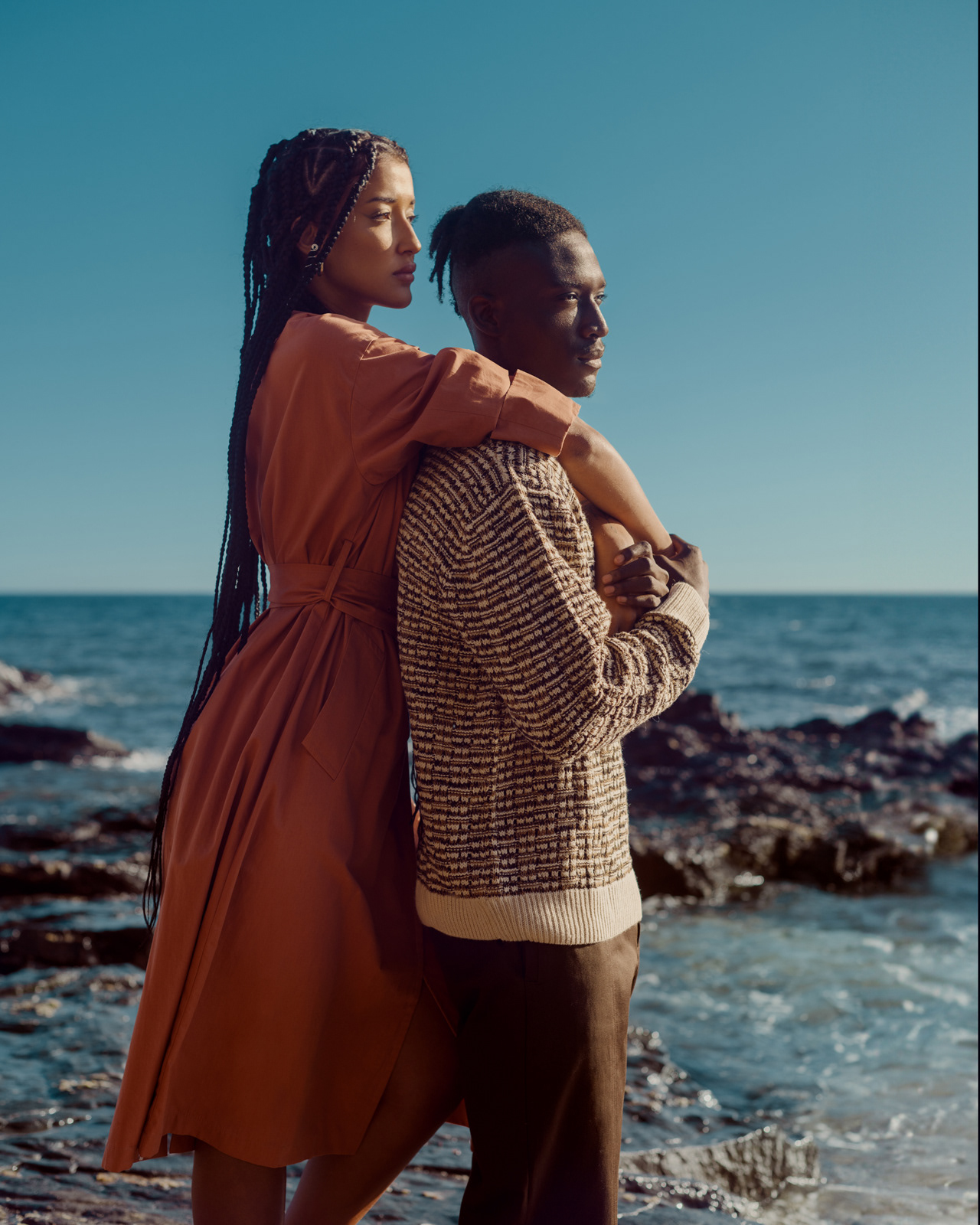 Editorial portrait of fashion couple standing on rocky shoreline – Joanna Kustra, destination fashion photography