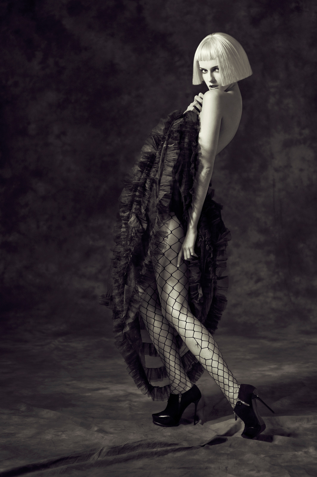 Black and white high-fashion editorial portrait of model in ruffled gown and fishnet tights – Joanna Kustra studio fashion photography