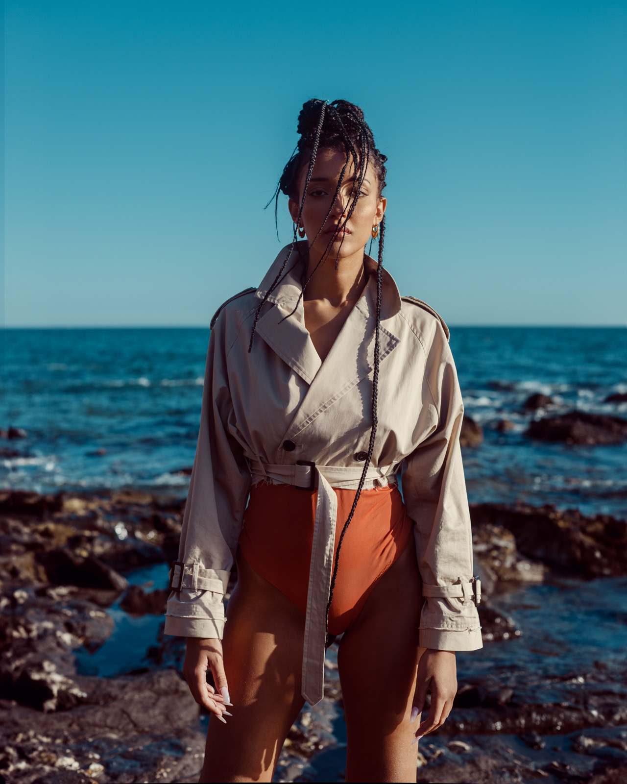 Seaside portrait of model in trench coat and orange bodysuit – Joanna Kustra coastal fashion photography