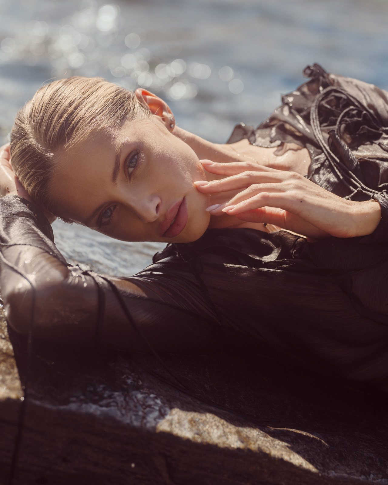Close-up beauty shot of model reclining on rocks in wet black dress – Joanna Kustra seaside fashion photography