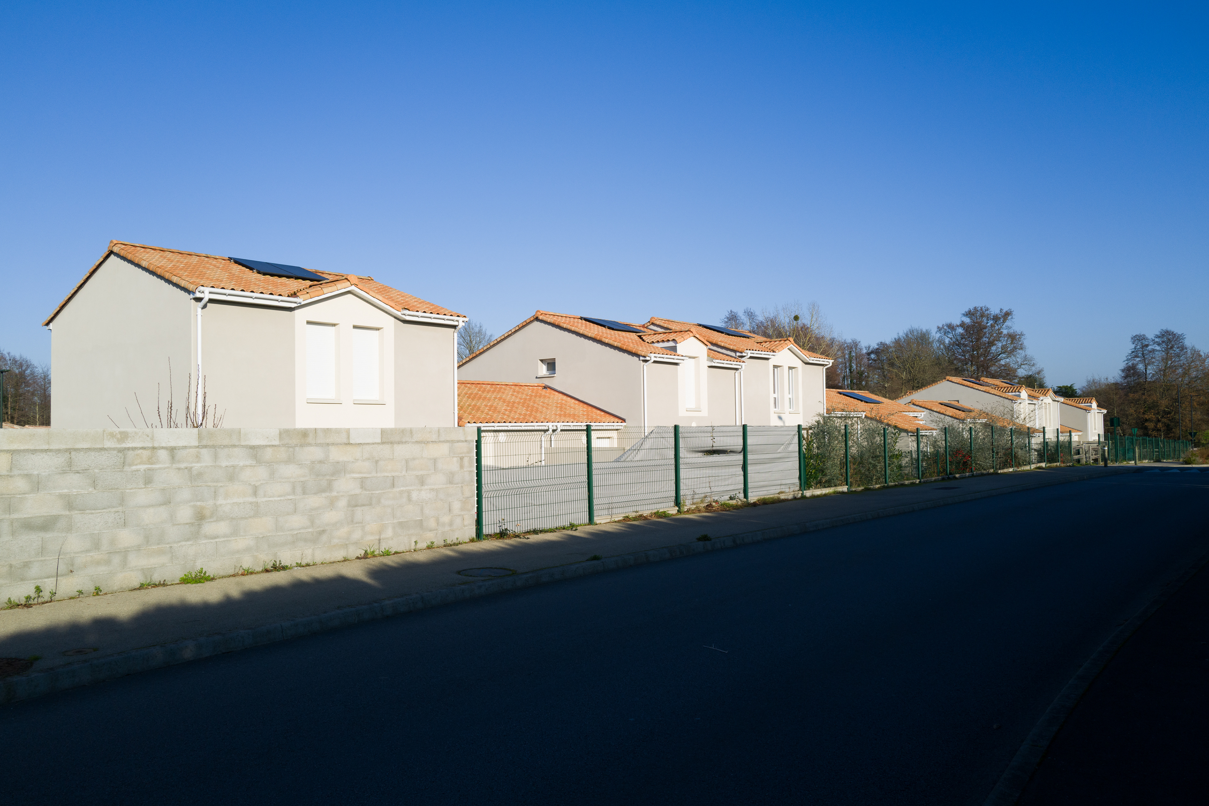 Des maisons neuves de type lotissements, alignées le long d'une route. Les maisons sont toutes les mêmes et les terrains sont bordés de murs en parpaings ou de clotures.