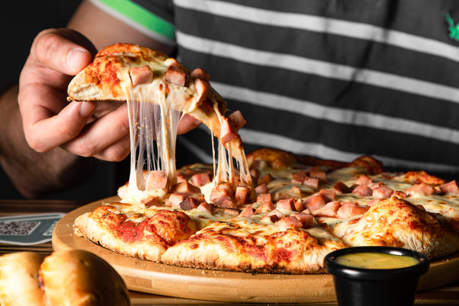 Persona levantando un pedazo de pizza dejando ver el queso derretivo