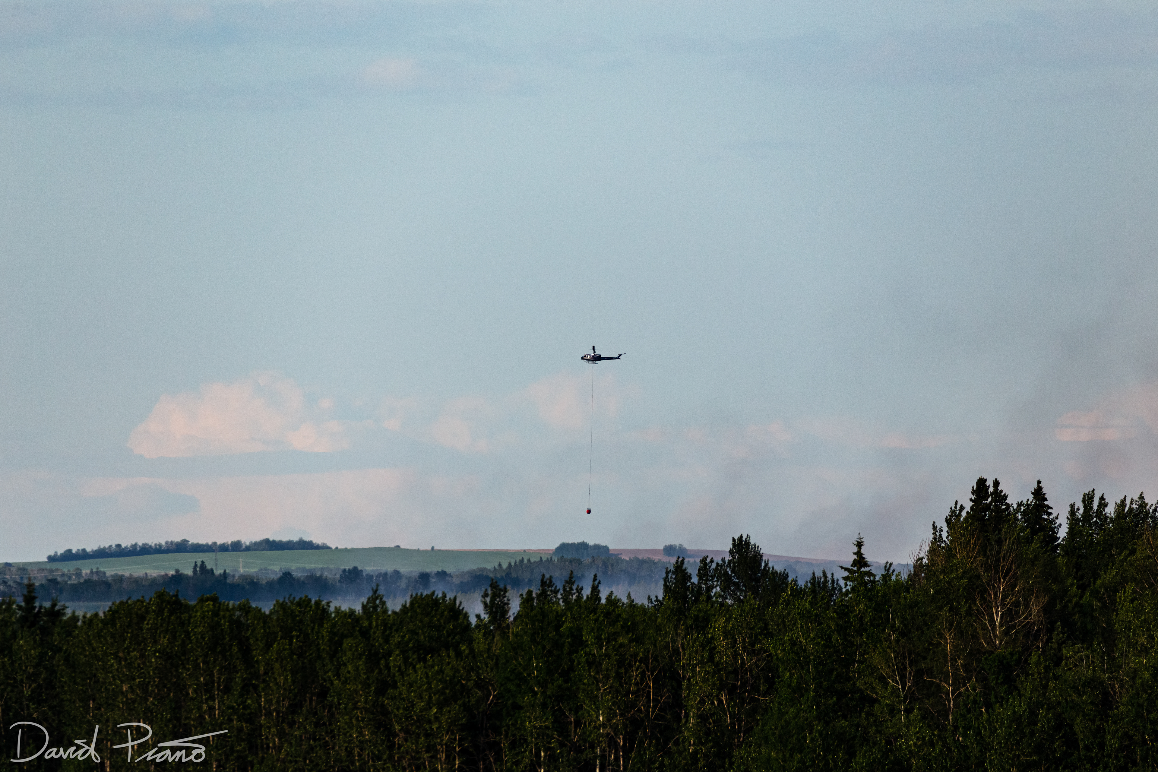 A bucket helicopter works over a raging wildfire in Yellowhead County, AB - June 2021
