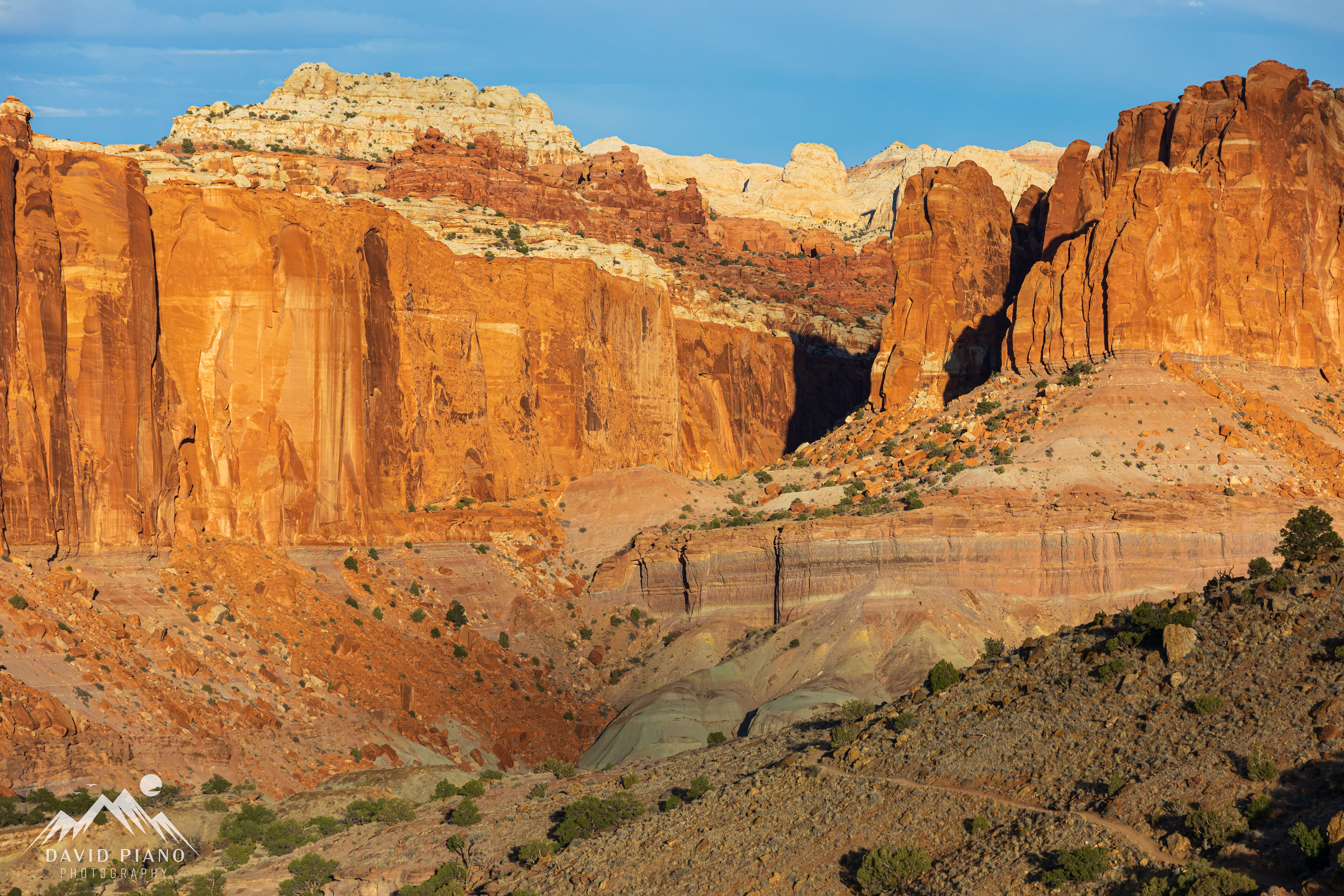 The late-day sun illuminates a sandstone escarpment viewed from the Chimney Rock Trail