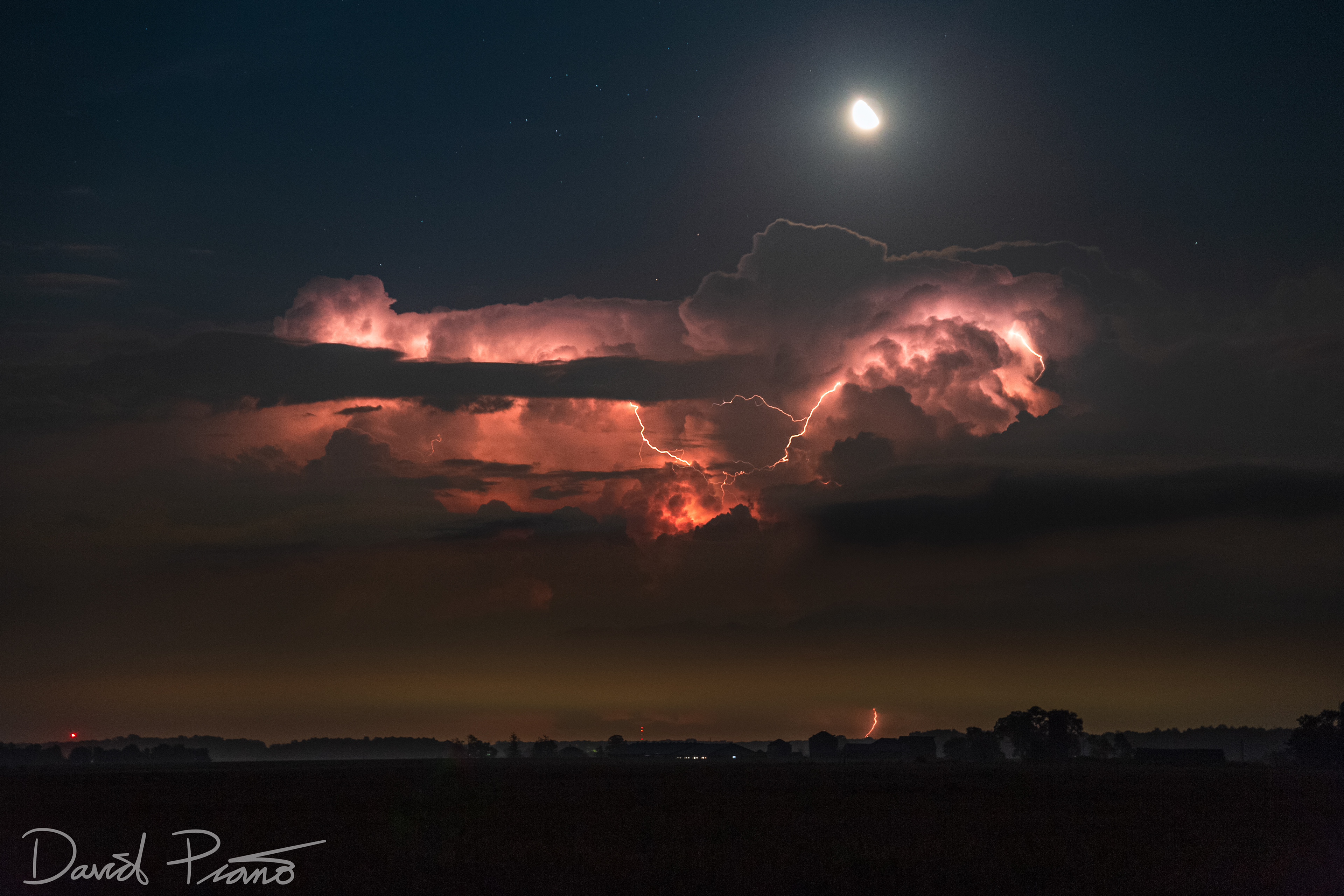The moon shines over a distant electric cumulonimbus