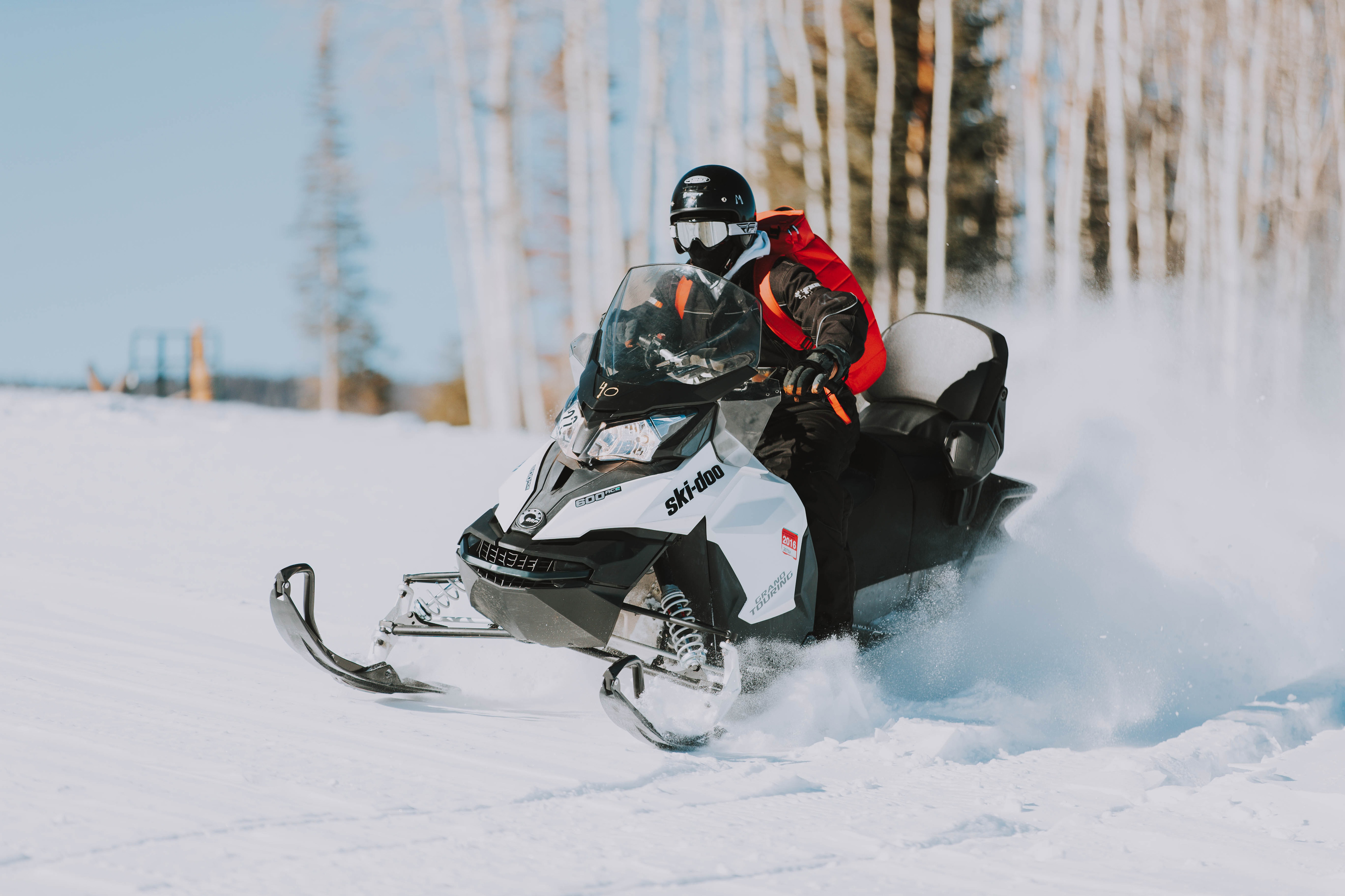 A person rides a snowmobile over fresh powder. They are wearing a helmet and goggles.