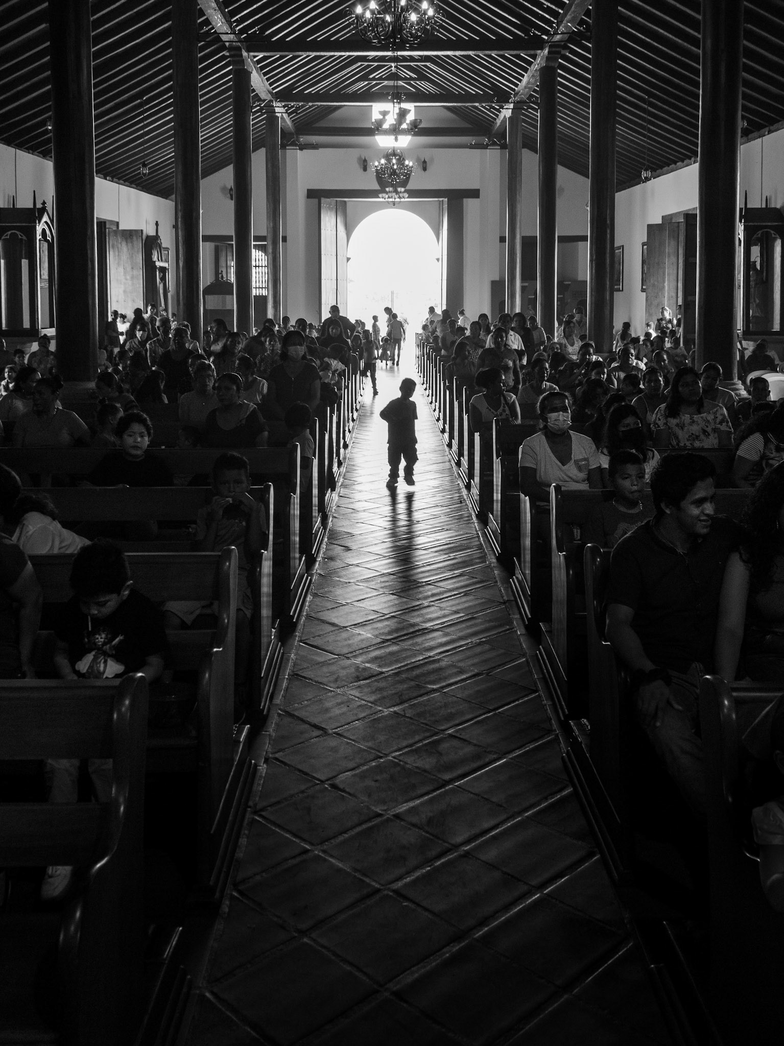 A child walks down the central aisle of the church, lit by the light from the entrance, in Diría, Pueblos Blancos, Nicaragua.