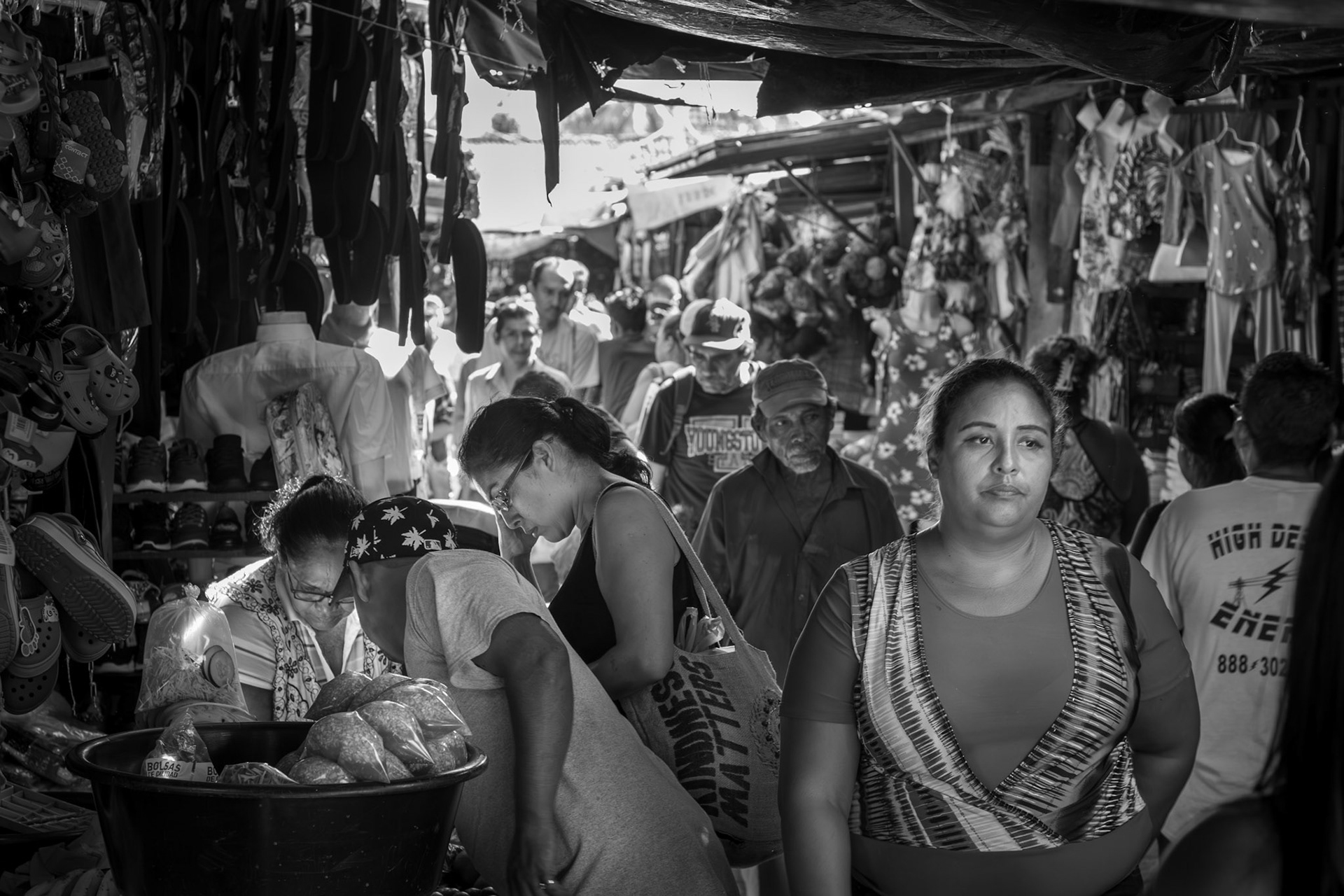 A woman walks through the busy market in Granada, Nicaragua, surrounded by vendors, shoppers, and hanging goods, as sunlight filters through the narrow aisles.