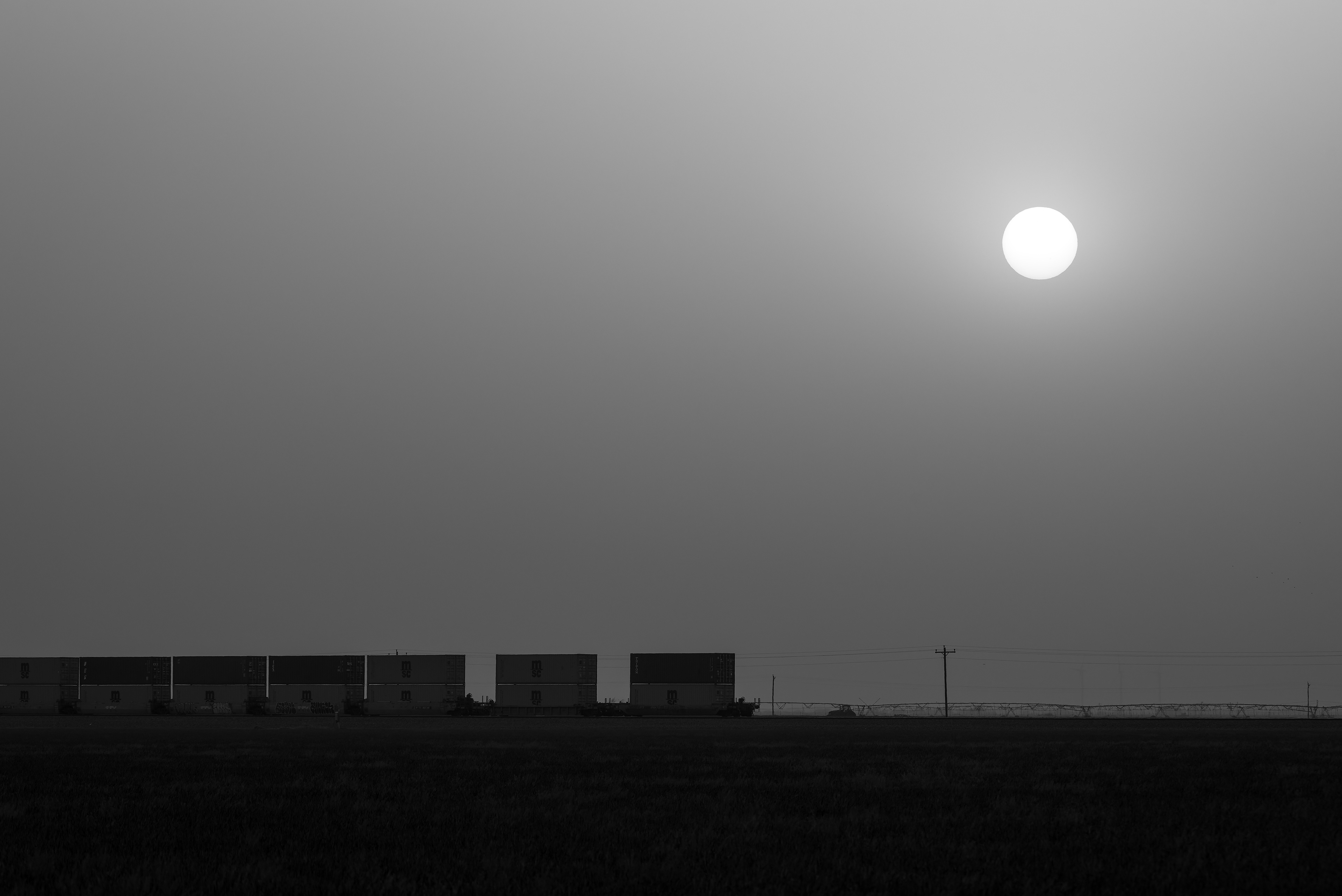 The setting sun hangs in a dust-filled April sky and watches over a westbound stack train that sits idle on the main at Black, Texas.