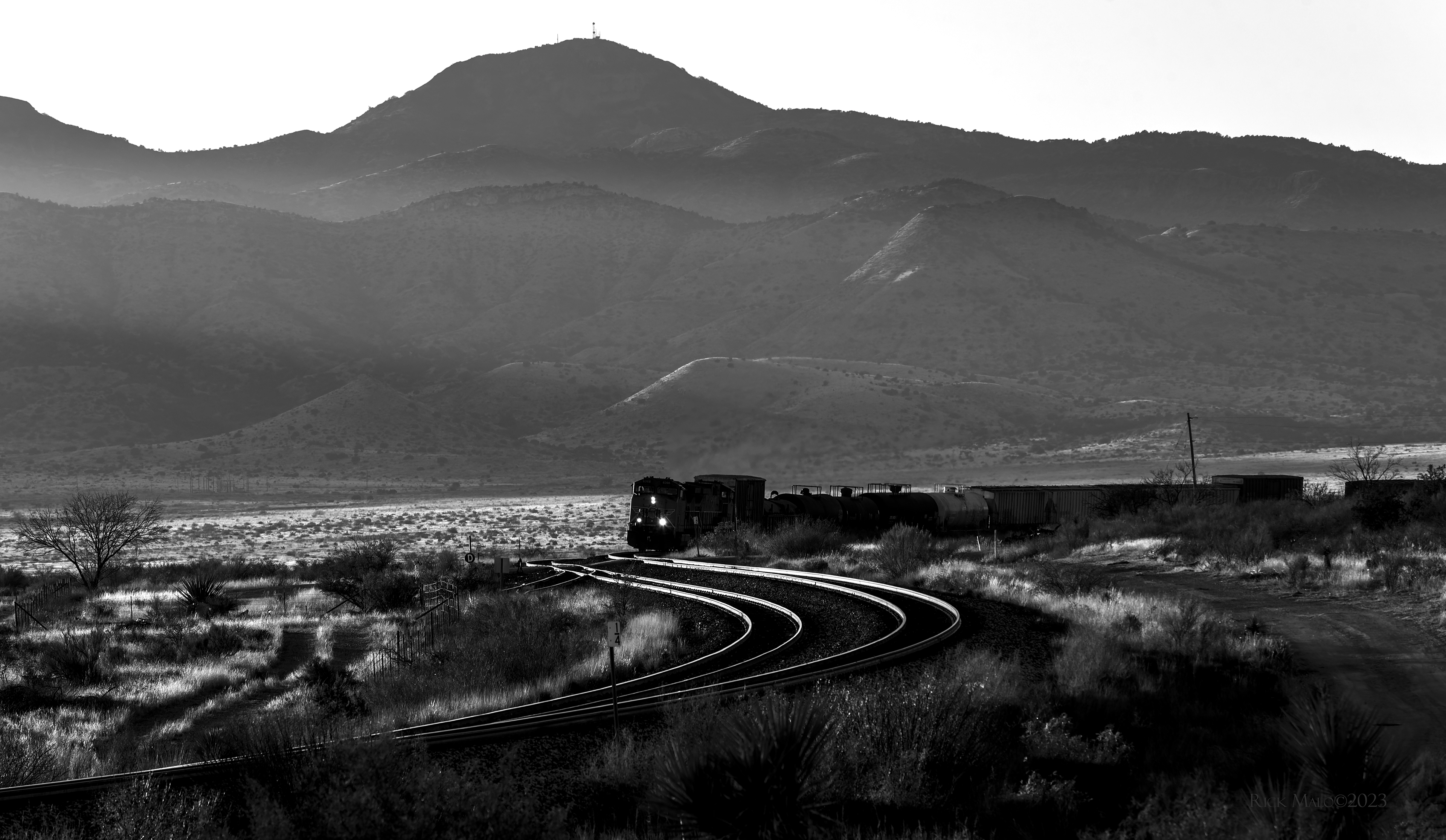 A dusty beam of light casts down into the valley of Dry Dugout Creek as the evening sun slips over the Del Norte Mountains of West Texas on a chilly December 2021 afternoon. The thugga-thugga-thugga-thugga sound of GEs laboring with a heavy train fills the valley as they roll into the curve at Lenox siding west of Marathon along Union Pacific's fabled Sunset Route.
