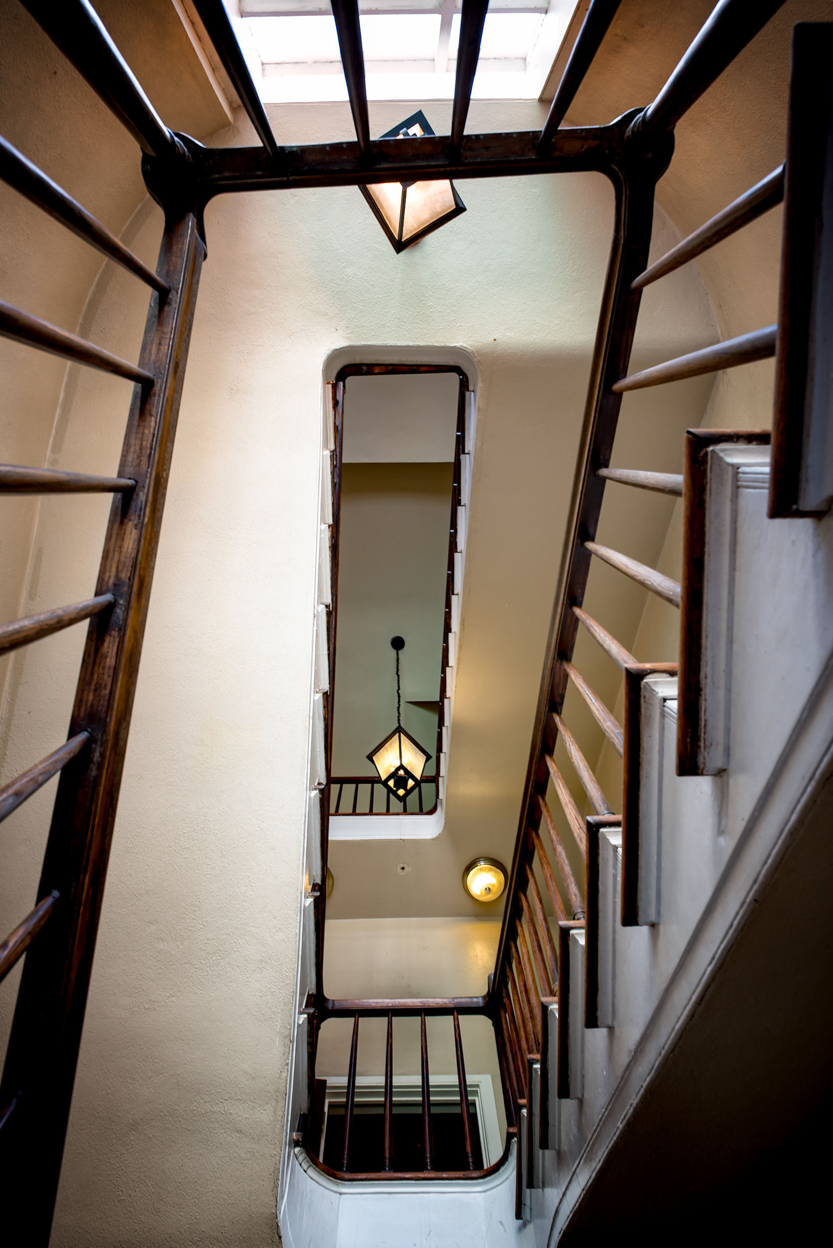 No idea whose stairwell this is — I never asked, and by the time it occurred to me to, I'd already been standing in someone's building longer than a stranger reasonably should. French Quarter townhouses run long and narrow, which starves the middle floors of light, so builders added stair towers like this one, with a skylight at the top pulling daylight down through every landing. Whoever's building this is, it's doing exactly what it was built to do.