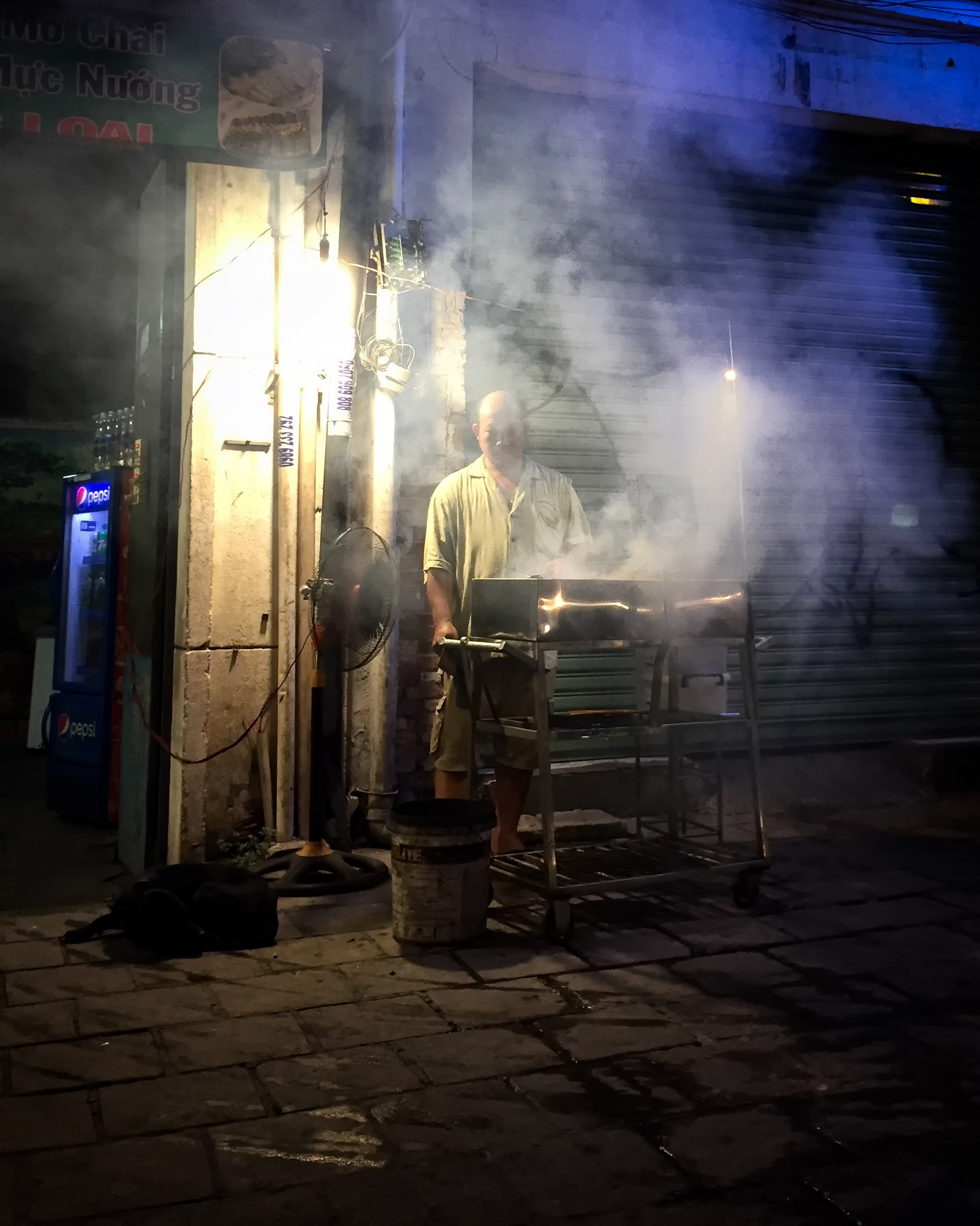 A street vendor grills bò lá lốt in an older residential district of Saigon — maybe District 3, though I'm not certain — beef wrapped in wild betel leaf and cooked over open flame until the whole block smells like it. Real betel leaf, the kind chewed with areca nut, is a different plant entirely — this one's just the fragrant cousin.