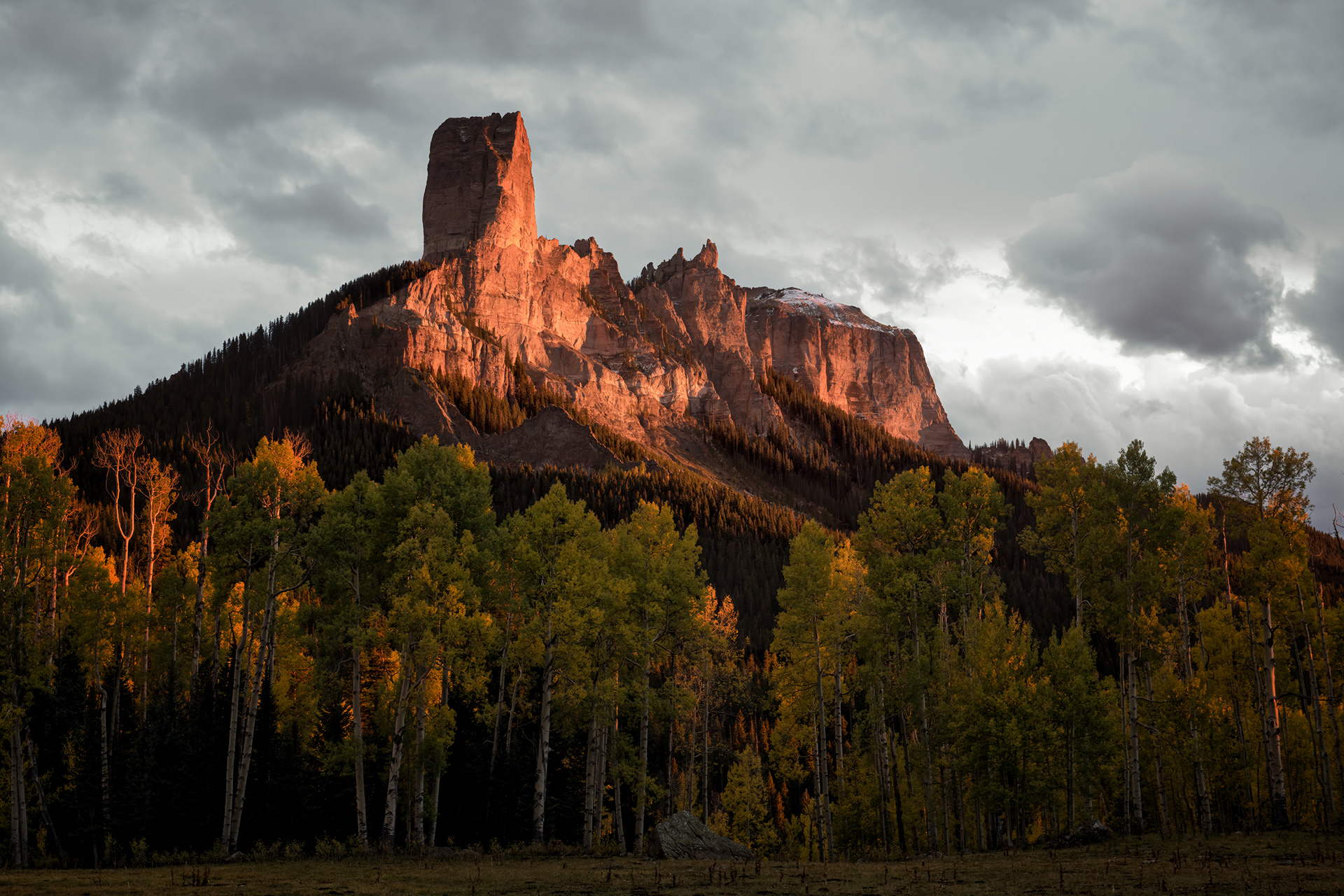 Two spires near Owl Creek Pass, catching what's left of the day's light — and Chimney Rock, the narrower of the two, has this genuinely strange, hyper-specific claim to fame worth just stating plainly: it's the steepest point in the entire state of Colorado, 61.4 degrees on average, i.e., 1,600 vertical feet gained over less than half a mile, a slope that's functionally closer to a wall than a mountain in any sense most people mean by "mountain." Nobody touched it until 1934, and the one route up it is still rated the same 5.6 it was rated then. It also has a film career, of all things — the skyline behind John Wayne in True Grit, and, before that, in How the West Was Won, both times uncredited, both times just standing there being steep.