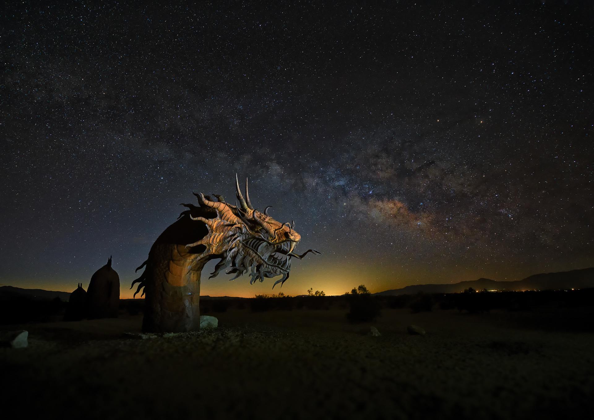 Galleta Meadows, before dawn — 350 feet of welded-metal dragon snaking through the sand under the Milky Way, a 20-second exposure at ISO 3200 doing the work a normal shutter never could. Most of the roughly 130 sculptures scattered across this private, unfenced estate are modeled on animals whose actual fossils were once dug out of this exact desert. The dragon isn't one of those — no fossil, no science, just a dragon. Made by Ricardo Breceda, a self-taught welder who started all of this by building his daughter a 20-foot Tyrannosaurus rex for Christmas because she'd just seen Jurassic Park III and asked.