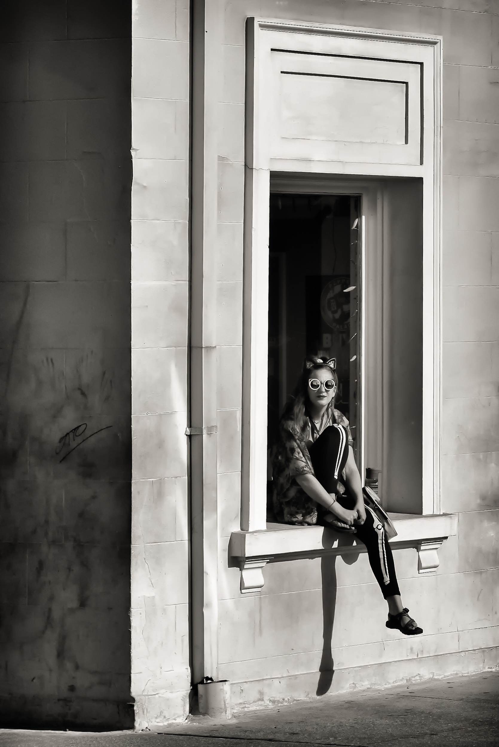 I don't know anything about her — not her name, not why she'd picked that window ledge to sit in like it was furniture, not whether she noticed me taking this before or after I'd already taken it. That's most of street photography, honestly: you get one frame of somebody's afternoon and none of the rest of it, and you're stuck making guesses about a person who owes you nothing and gave you nothing except, in this case, a very good hat.