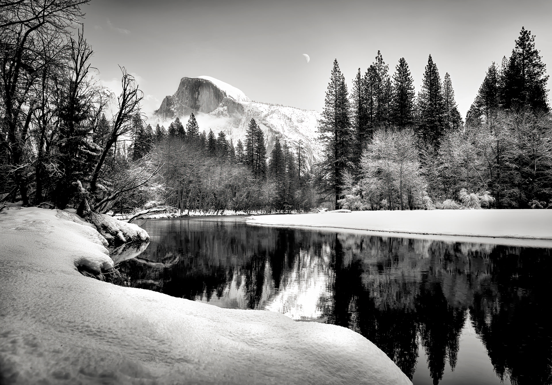 Half Dome isn't missing a half — never was, actually, though try telling that to your eyes right now (they're very committed to the bit). From the valley it reads like something sheared it clean off, but geologists figure as much as 80 percent of that "missing" northwest face might still be sitting right there; what you're seeing is a thin ridge of rock turned edge-on, ordinary erosion and jointing taking credit for what looks like one catastrophic decision. That's a crescent moon parked just off the summit, by the way, doing exactly what it does every day whether or not the sun's out to make it feel awkward about it — daytime moons aren't rare, we just don't look up enough to catch one. The Ahwahneechee called the dome Tis-sa-ack. Those dark streaks are lichen. One older account insists they're a young woman's tears instead, and of the two explanations, I know which one I'd rather have caption duty on