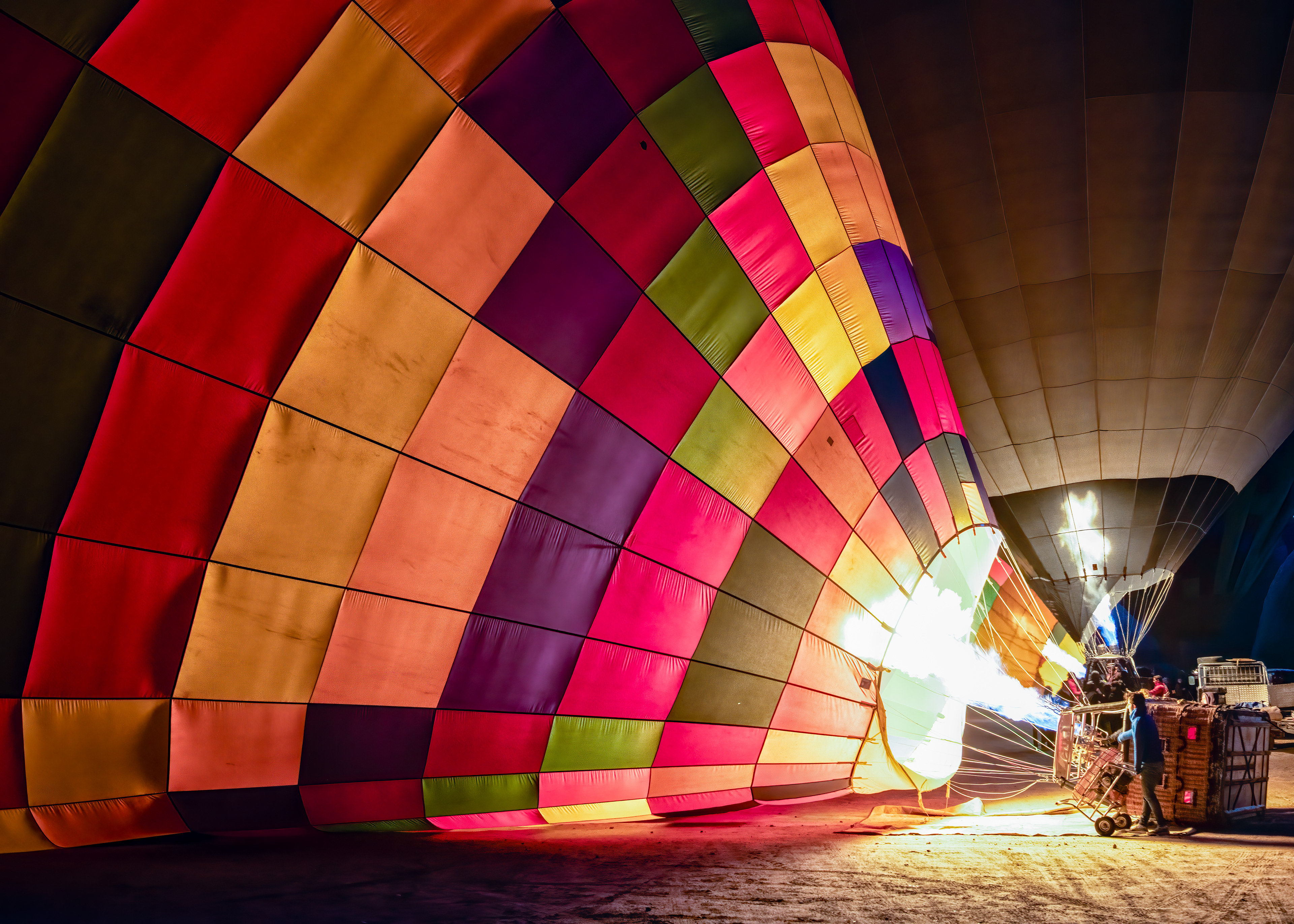 Cappadocia balloon, mid-inflation, burner firing straight into the fabric. Ballooning here only started in 1991, and now something like 150 balloons lift off on a good morning, always before sunrise — the coldest air of the day is also the densest, which is what actually gives a balloon its lift, so the whole spectacle is scheduled around physics, not aesthetics. A few minutes earlier this was just a few thousand square feet of nylon lying flat on the ground.