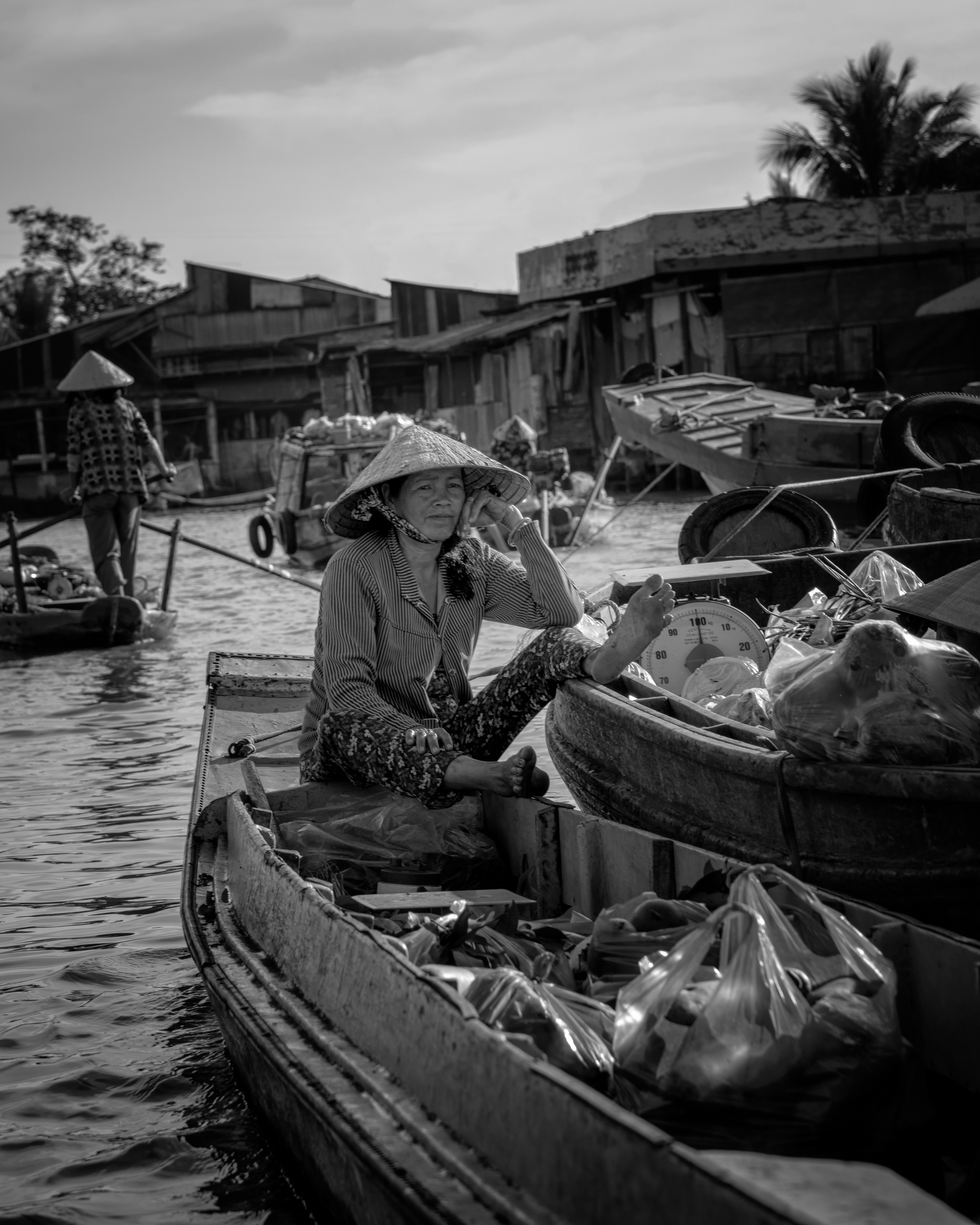 Cai Rang floating market, mid-morning. A vendor sits with her produce bagged and ready, the scale hanging beside her — but the buyers hadn't shown up yet. It was already warm, and she looked like she'd been waiting a while.