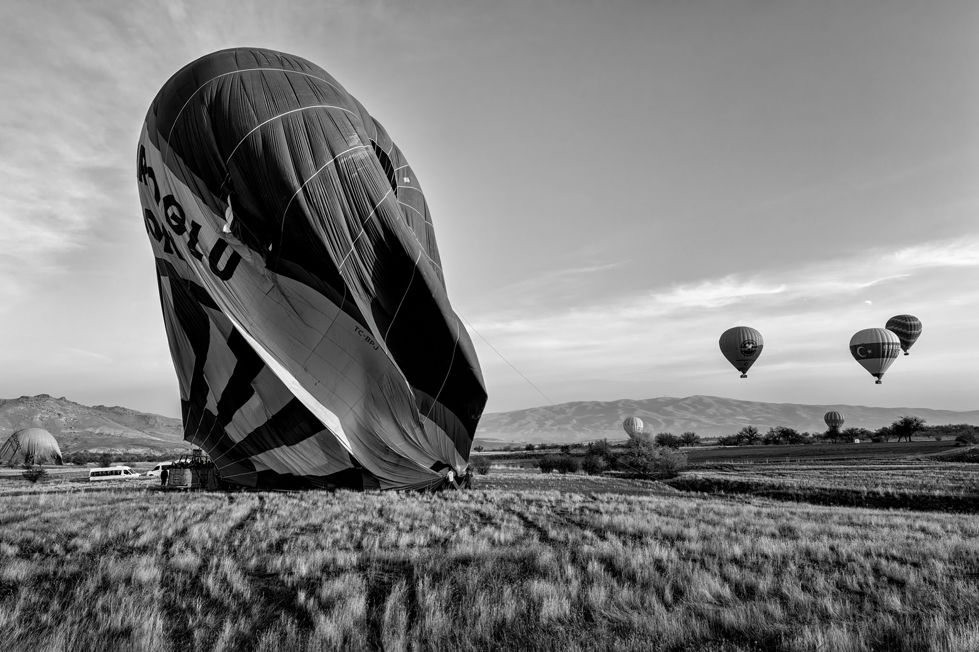Deflation, not just descent. Landing pulls a parachute vent open at the crown of the envelope — a panel that swings fully open instead of just easing shut, so what took twenty minutes to inflate collapses in under one. Whatever field it happens to land in is where it stays until the ground crew arrives to fold it. Tradition holds that a champagne toast follows every flight here, a custom that supposedly traces back to eighteenth-century France, when early balloonists kept landing, uninvited, in random farmers' fields and needed something better than an apology to hand over.
