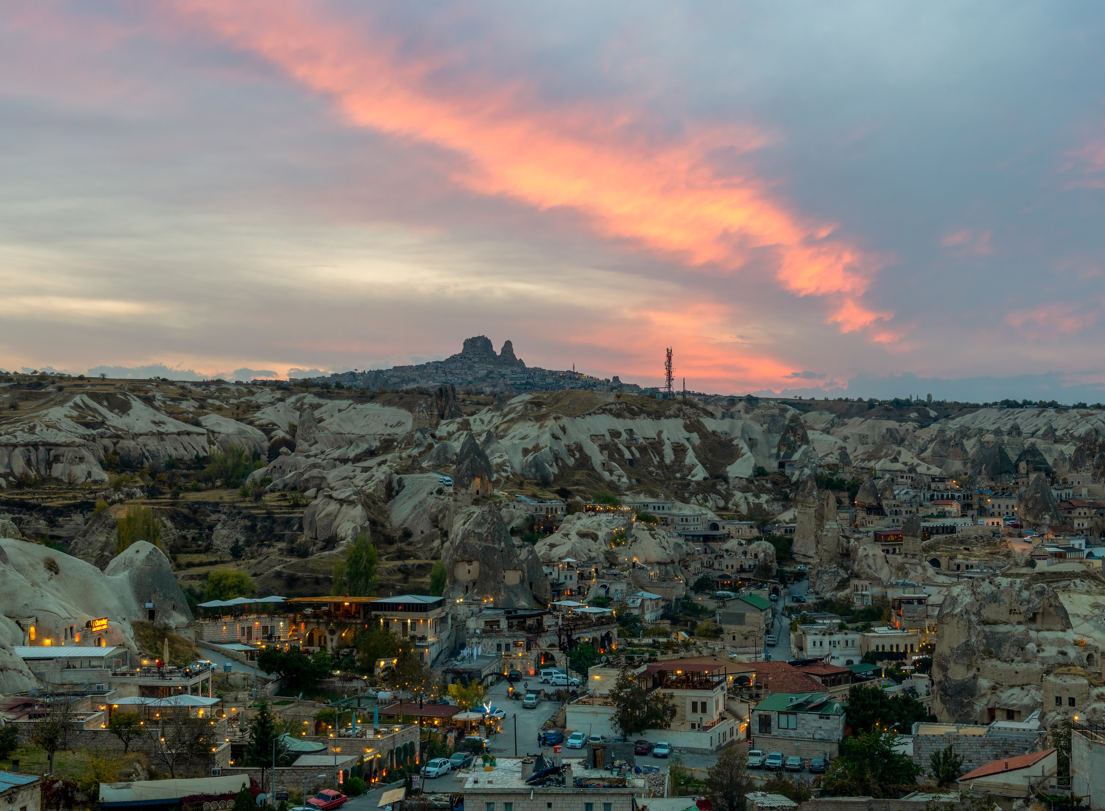 Uçhisar Castle at dusk, in silhouette — the tallest fairy chimney in Cappadocia, 196 feet of volcanic rock, carved rather than built, hollowed by hand over centuries into a warren of rooms and tunnels that once held as many as a thousand people. Nobody lives inside it now. The rock itself is soft enough to carve with hand tools and hardens once exposed to open air, which is the entire reason this region is riddled with places just like it