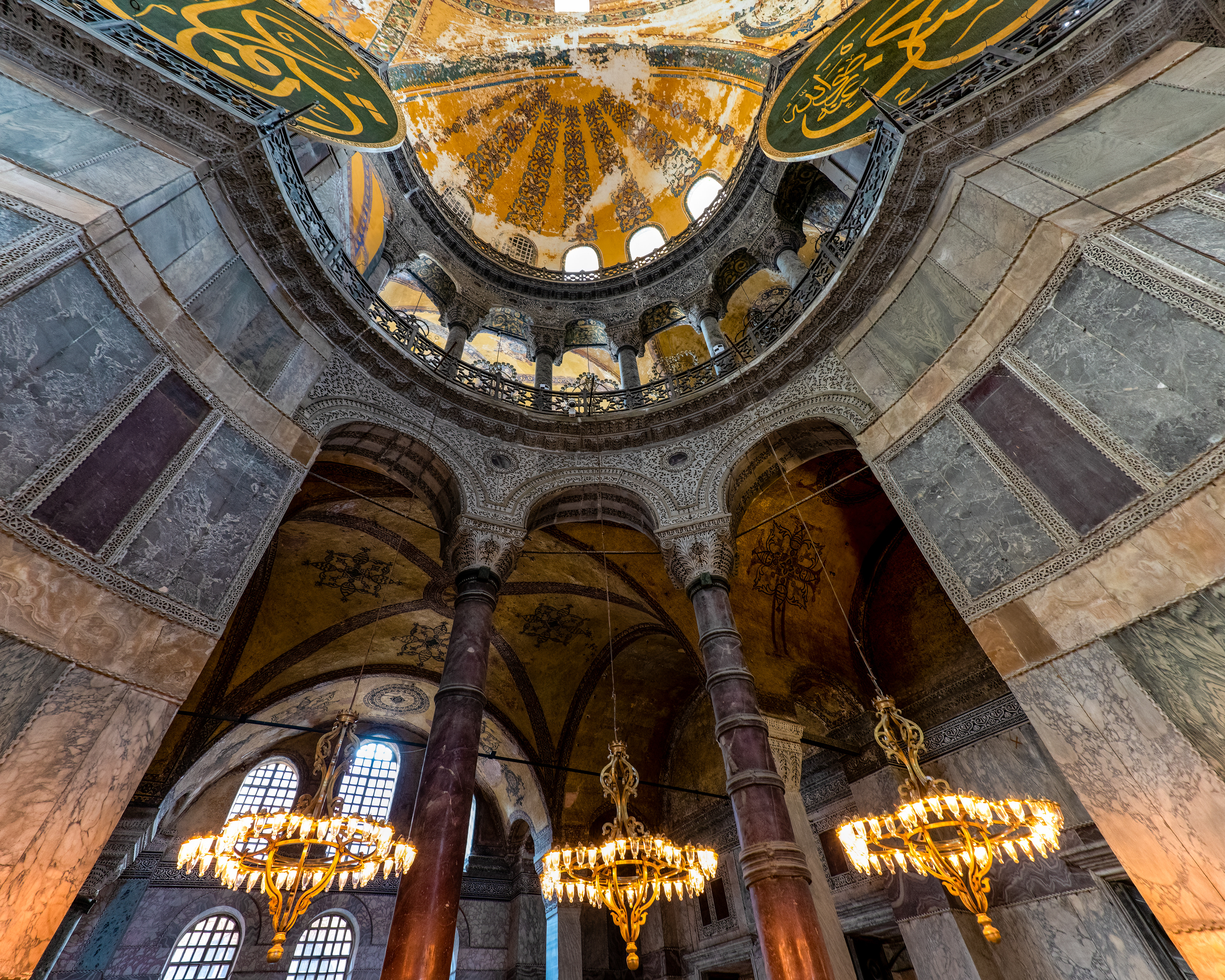 Hagia Sophia, dome and columns. A hundred and forty columns hold this place up, and almost none of them were built for it — eight purple porphyry ones came from Egypt, eight green ones from the Temple of Artemis at Ephesus, one of the ancient world's Seven Wonders, repurposed rather than replaced. No two capitals match. Near the northwest exit there's a "sweating column" people still put a thumb into and twist, on the belief that if it comes back damp, whatever they wished for is coming