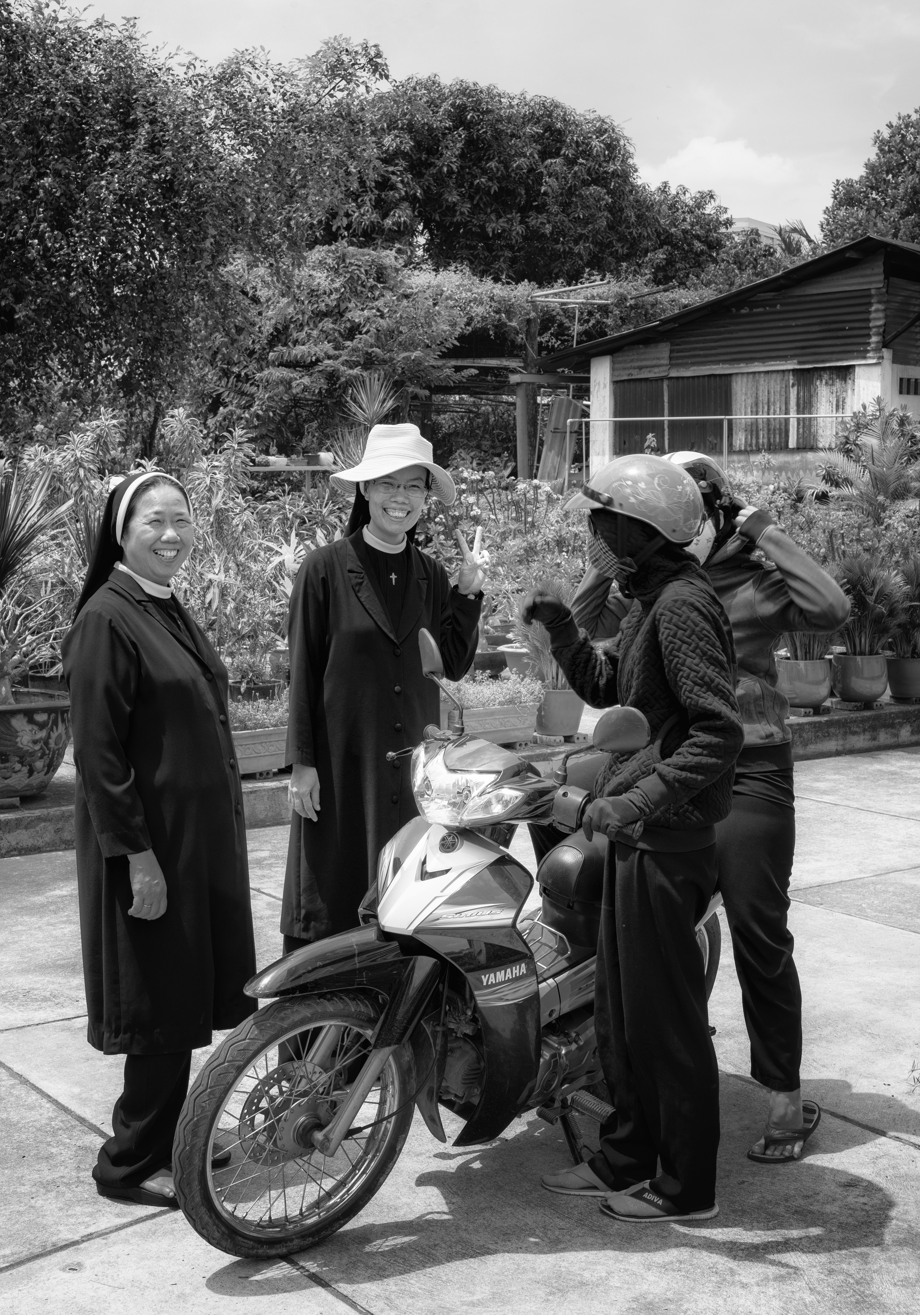 Saigon, 2018 — my aunt's Jubilee, call it Golden (fifty years, more inference than fact), though nobody actually confirmed it. Meanwhile, unbothered by any of this: two sisters laughing, one throwing up a peace sign, two more half in their helmets, ready to ride off like none of it happened.