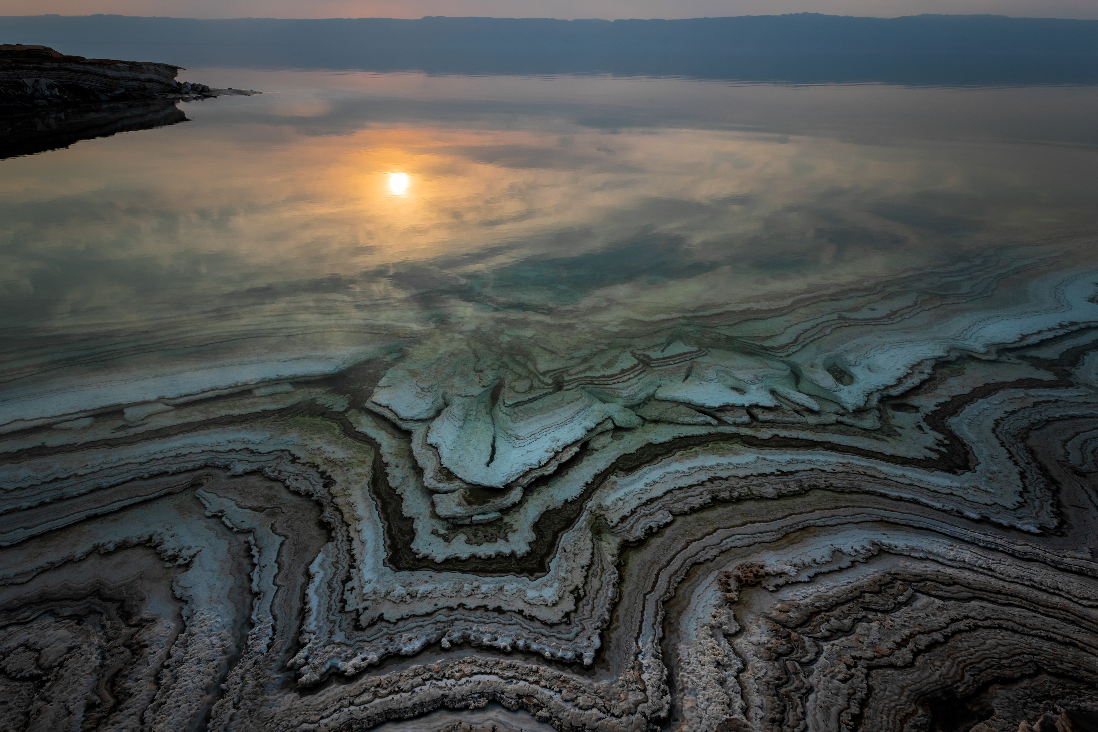 Dead Sea, sunrise. Ten times saltier than the ocean. Nothing lives in it, only salt. We stayed on the shore two days and rubbed the mud into our skin. I swam out and floated — you cannot sink here, not even trying. Each year the water pulls back a little more, and leaves these terraces behind