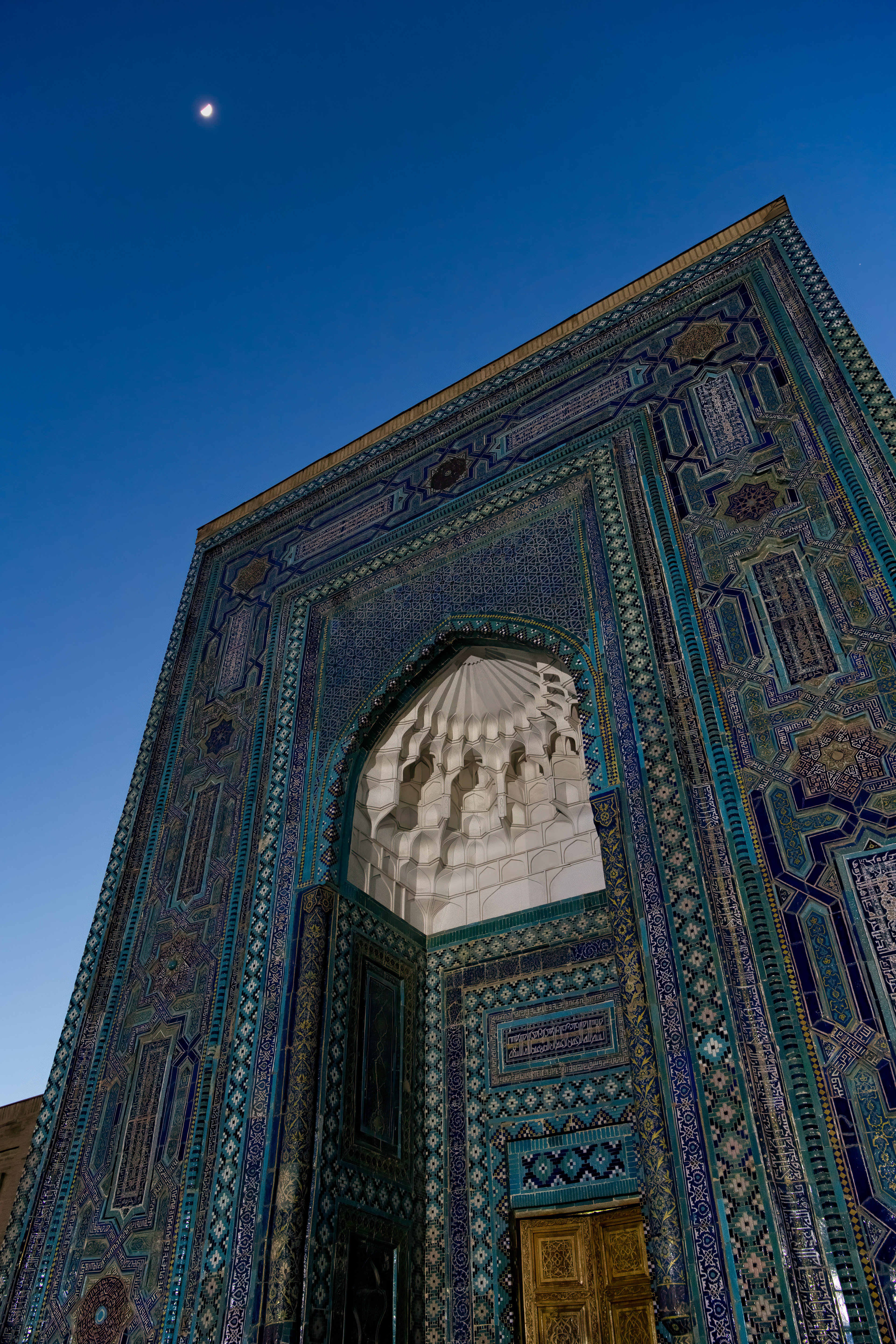 Shah-i-Zinda means "the Living King," named for Qutham ibn Abbas, a cousin of the Prophet Muhammad who — according to the story, and I want to be clear this is the story, not a claim — was beheaded mid-prayer, picked up his own head, and walked into a well here, where he's said to still be living. Whatever you make of that, people have been building tombs around it for eight centuries. The moon just happened to be up when I was.