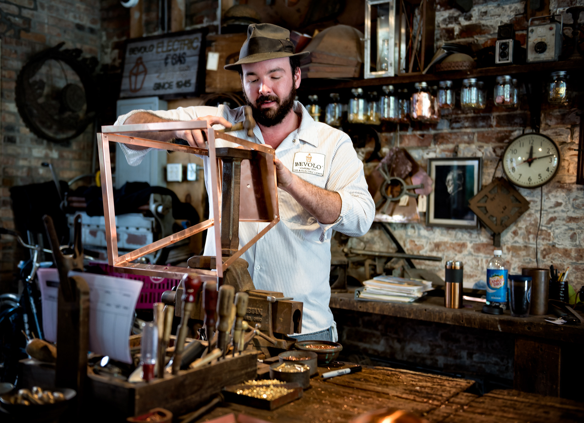 This is a Bevolo lantern going together, hand-riveted rather than soldered, which is the whole point of the company — solder gives out eventually in this climate, rivets don't. Andrew Bevolo Sr. started the business in 1945 after working for Andrew Higgins, the New Orleans boat builder who spent the war turning out the landing craft that got the Army onto beaches at Normandy and Iwo Jima. Bevolo took that same practical, built-to-outlast-you sensibility and pointed it at copper gas lamps instead. Eighty years later his grandson runs the company, and the lanterns hanging over half the balconies in the French Quarter and the Garden District came out of a shop that still looks more or less like this one.