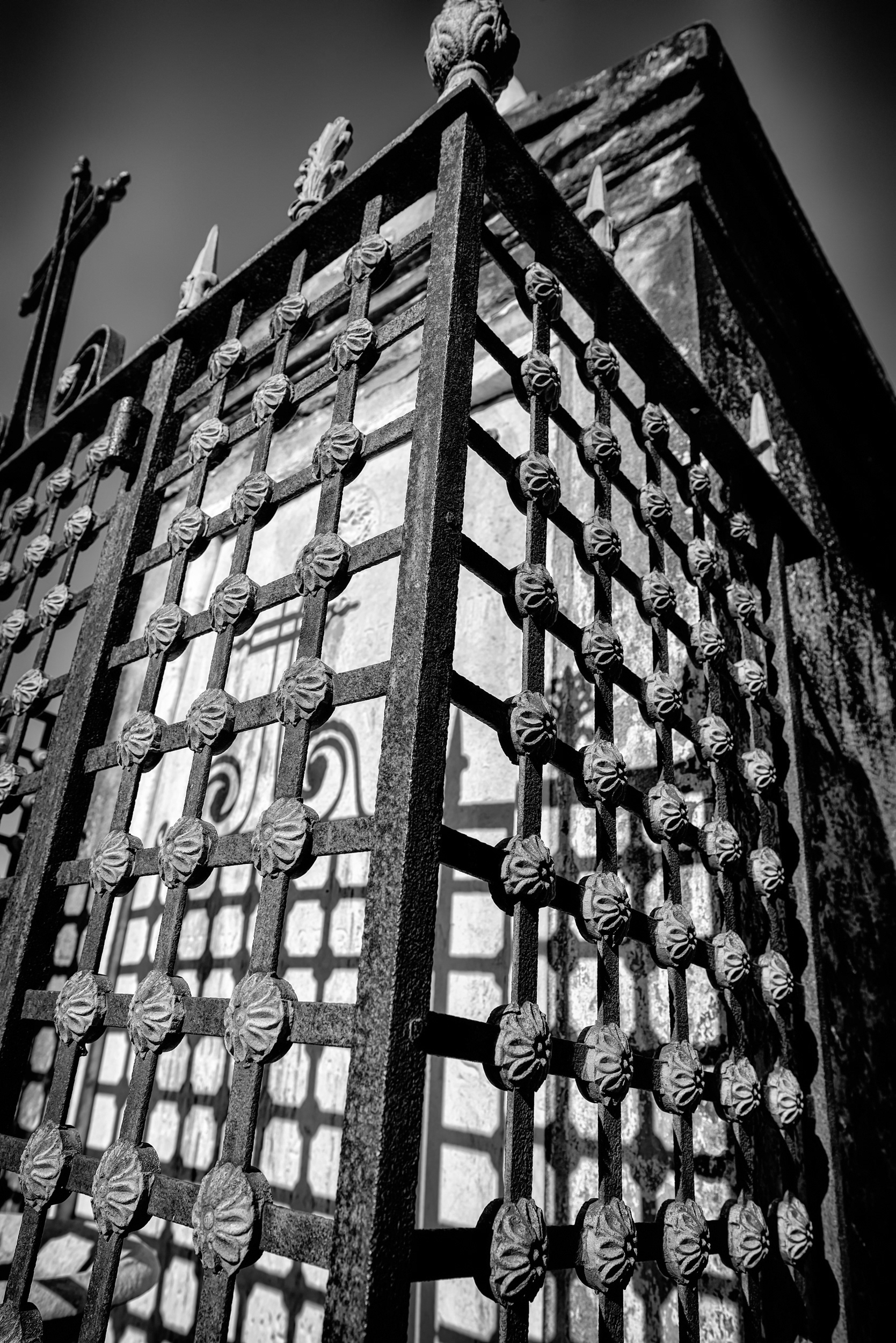 An iron security grille bolted over a tomb front — common in New Orleans cemeteries, where marble tablets and decorative ironwork have a long history of walking off. The city's ornamental ironwork tradition runs deep (inverted torches for the eternal soul, gryphons for guardianship), but this one's plain enough to suggest it was built to do a job, not be admired.