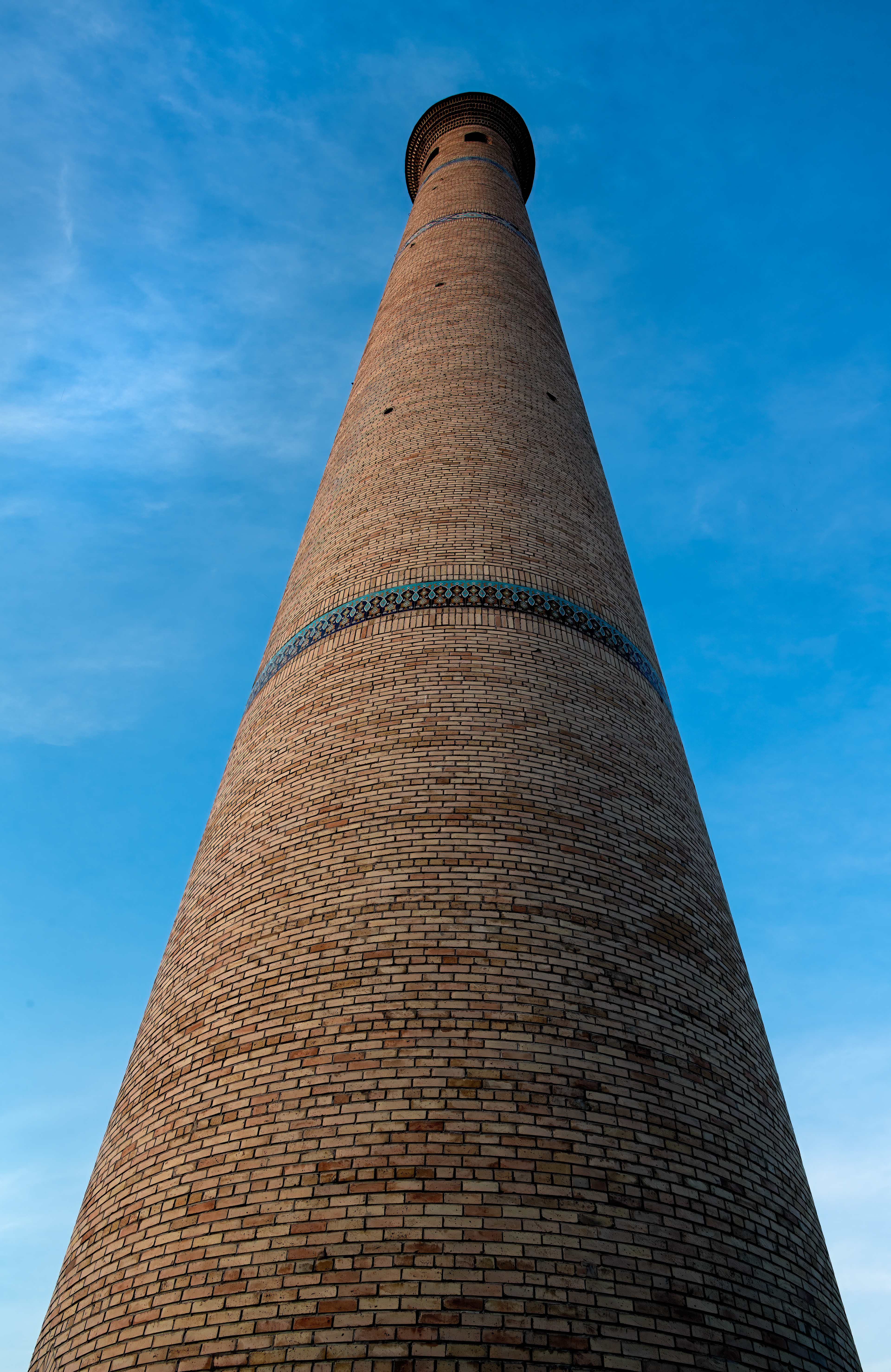 Built in 1127, the Kalyan Minaret has stood watch over Bukhara for nine centuries — long enough that Genghis Khan, of all people, ordered it spared when he leveled everything else around it. It earned a darker nickname later, the Tower of Death, for what got thrown from the top. None of that shows here. Just brick, sky, and a turquoise band circling the tower like it's holding its breath.