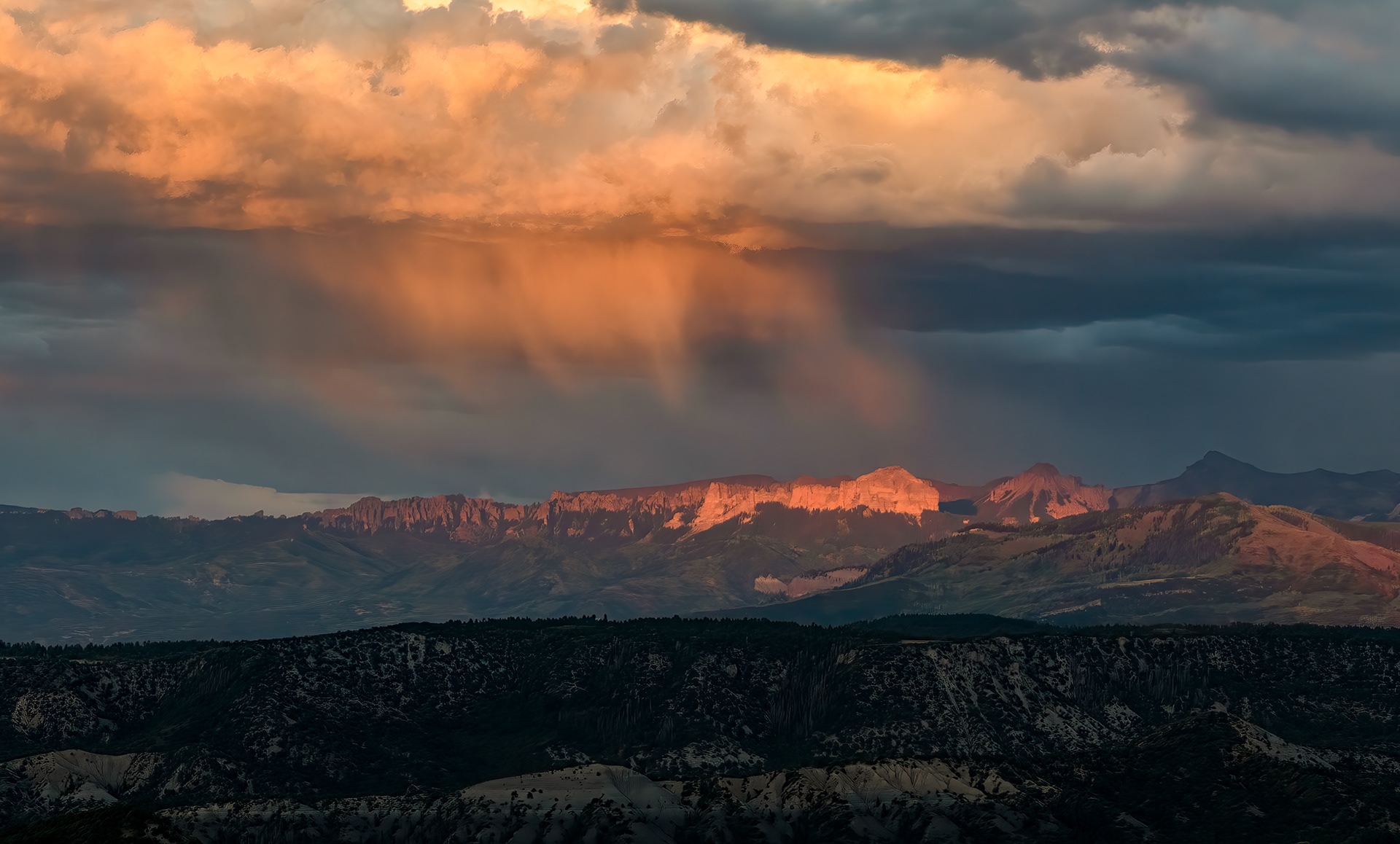 Virga, lit orange by low sun — rain that's already falling and already losing the fight before it reaches the ground. At elevation, the air near the surface is often dry enough that real moisture can be falling from a cloud a few thousand feet up and simply evaporate before any of it reaches the peaks below, leaving these curved, comet-like streaks instead of an actual storm. It's not purely decorative, either: virga is one of the more reliable ways lightning ends up starting a wildfire in the West, since a storm can build up enough charge to discharge without ever delivering the rain that would otherwise put the strike out.
