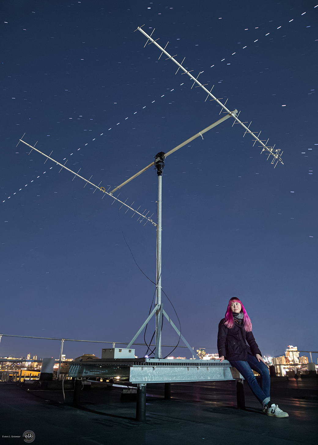Hannah Tomio and an antenna used to communicate with CubeSats on orbit on MIT building 37. The international space station passes overhead and Orion's belt is visible towards the right edge of the image.