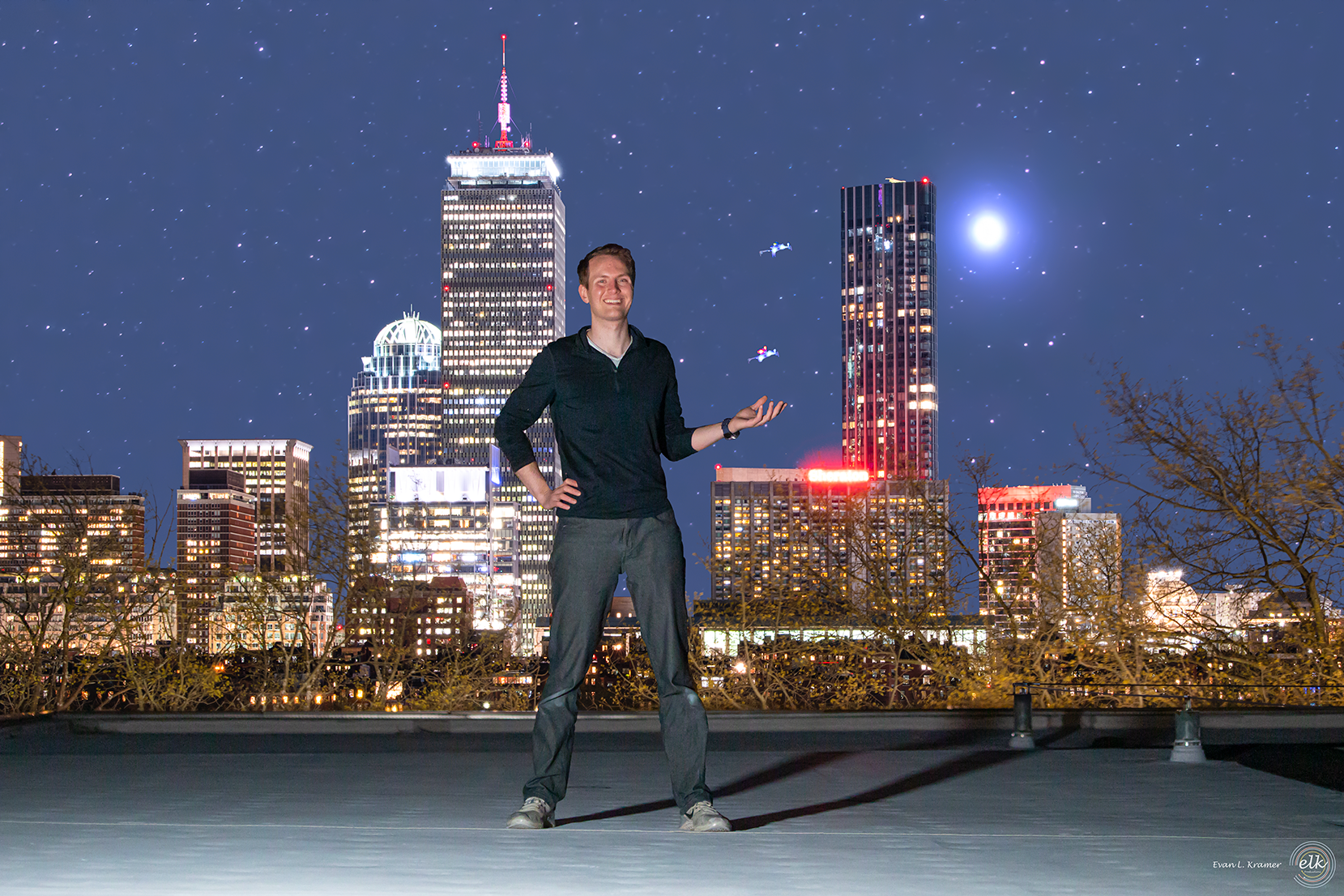 Charles Dawson and two drones atop MIT Building 3, Boston skyline, starscape, and Jupiter behind him. Six images were combined: Charles, lighting, drones, skyline, stars, with fog filter and long lens used for effect.