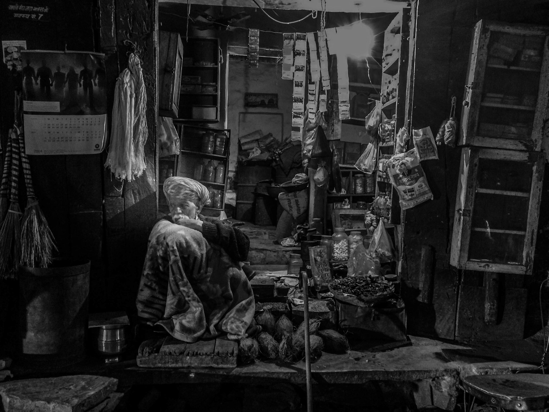 An old man in India, waits in his old shop in the cold night.