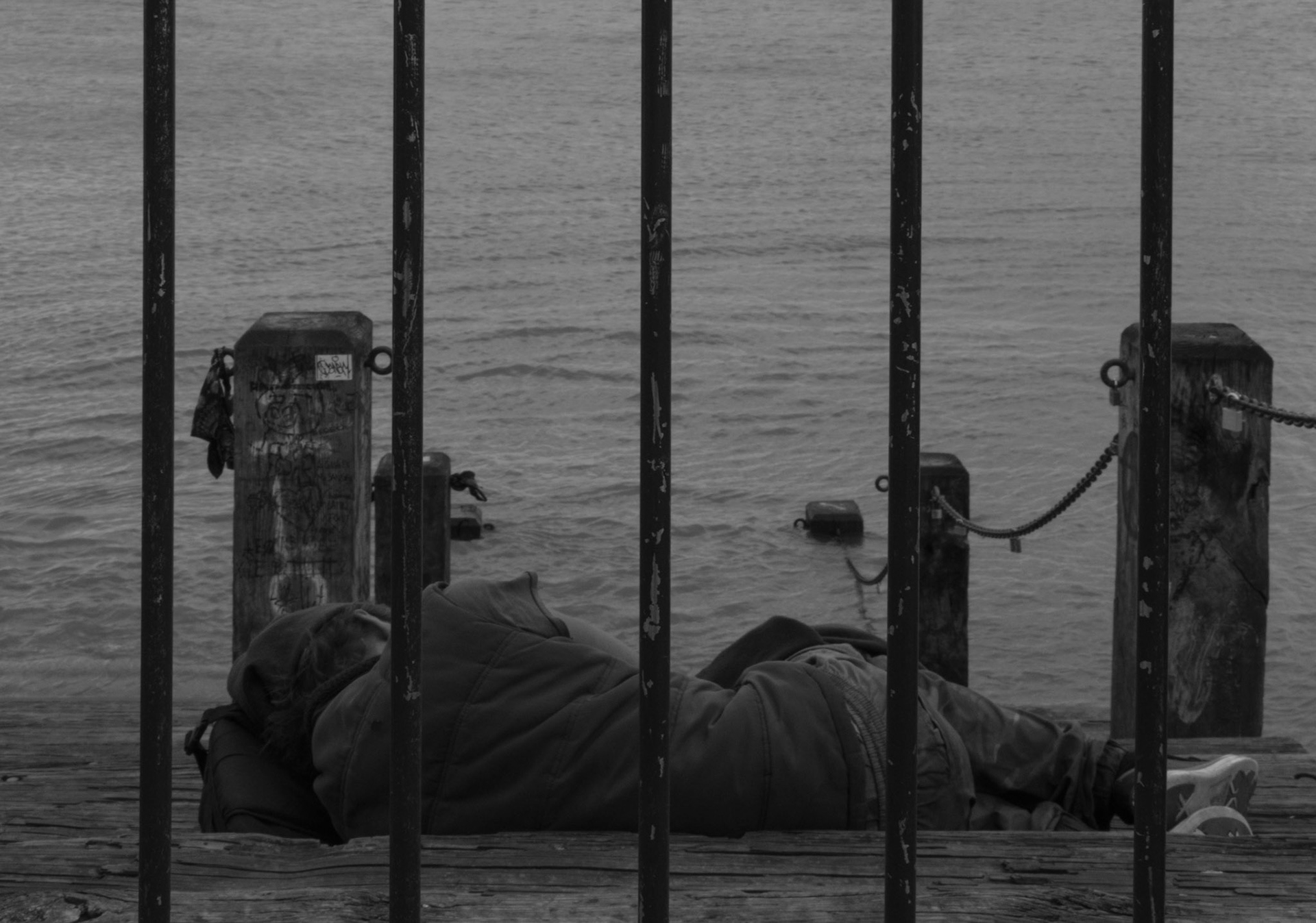 A homeless person in New Orleans, sleeps by the great Mississippi. The bars are a protection for the rest of us. Maybe paying for residences for homeless people is less important than for-profit incarceration.