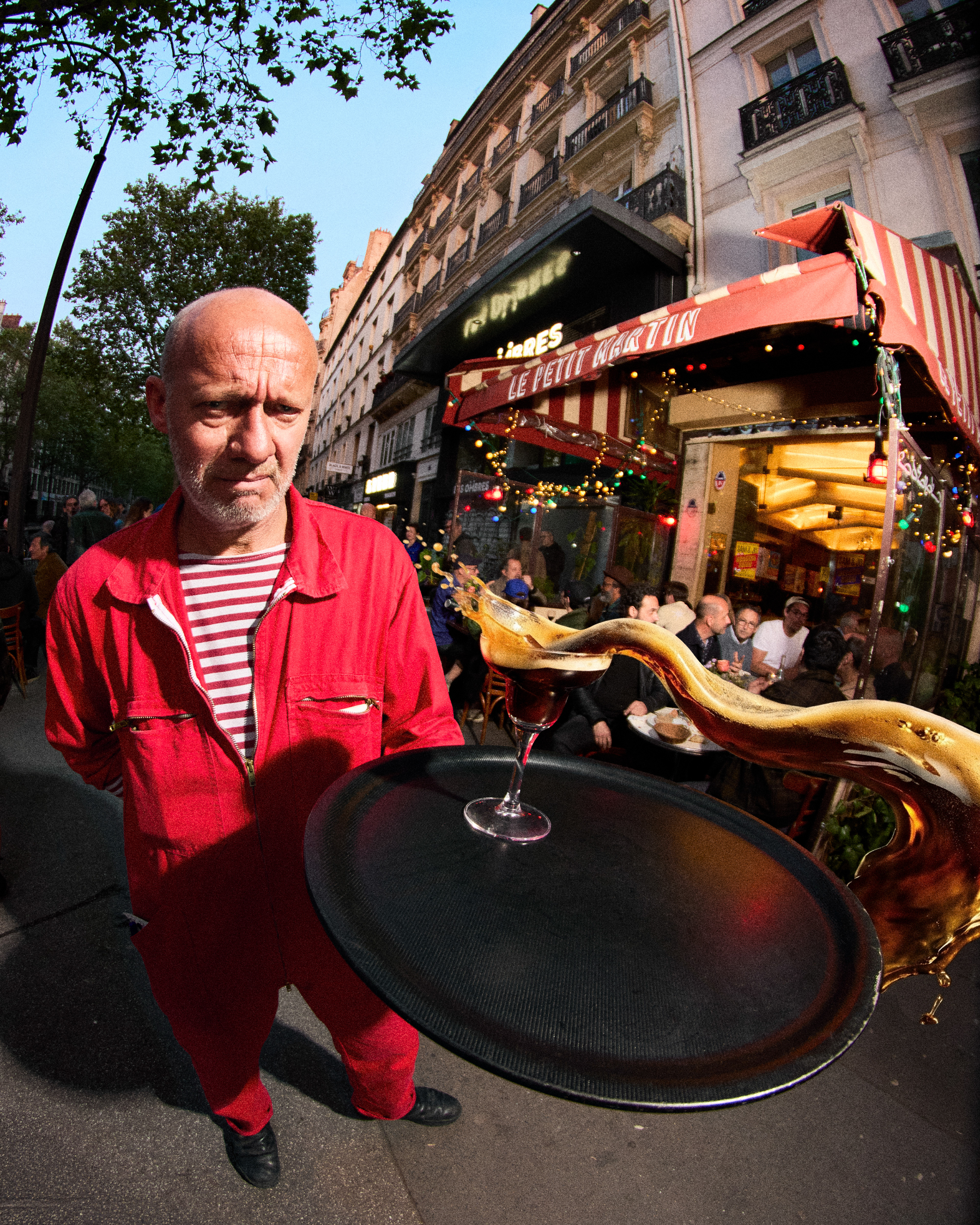 Serveur en combinaison rouge et plateau, éclaboussure de cocktail, terrasse de brasserie parisienne